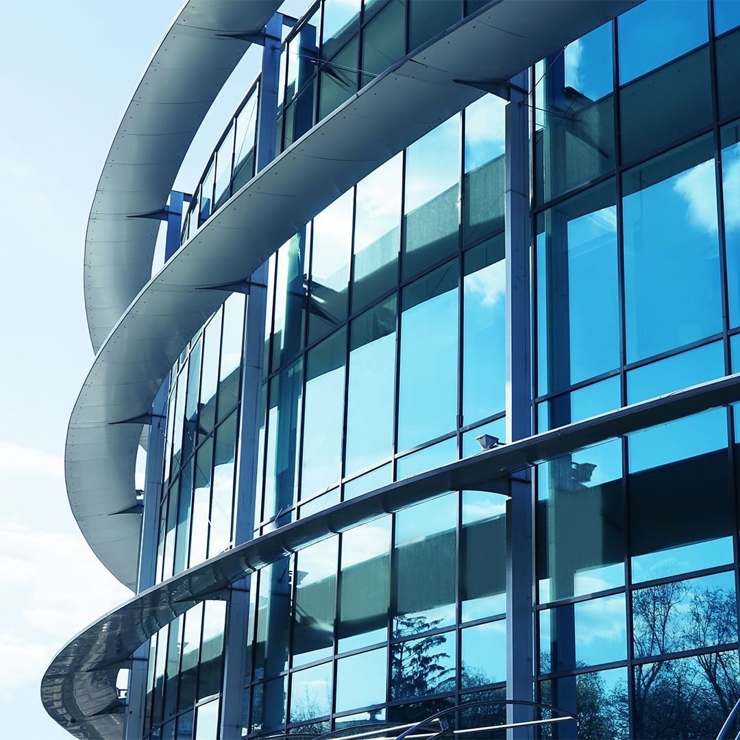 Modern, curved building with glass windows reflecting the sky. Blue and white tones.
