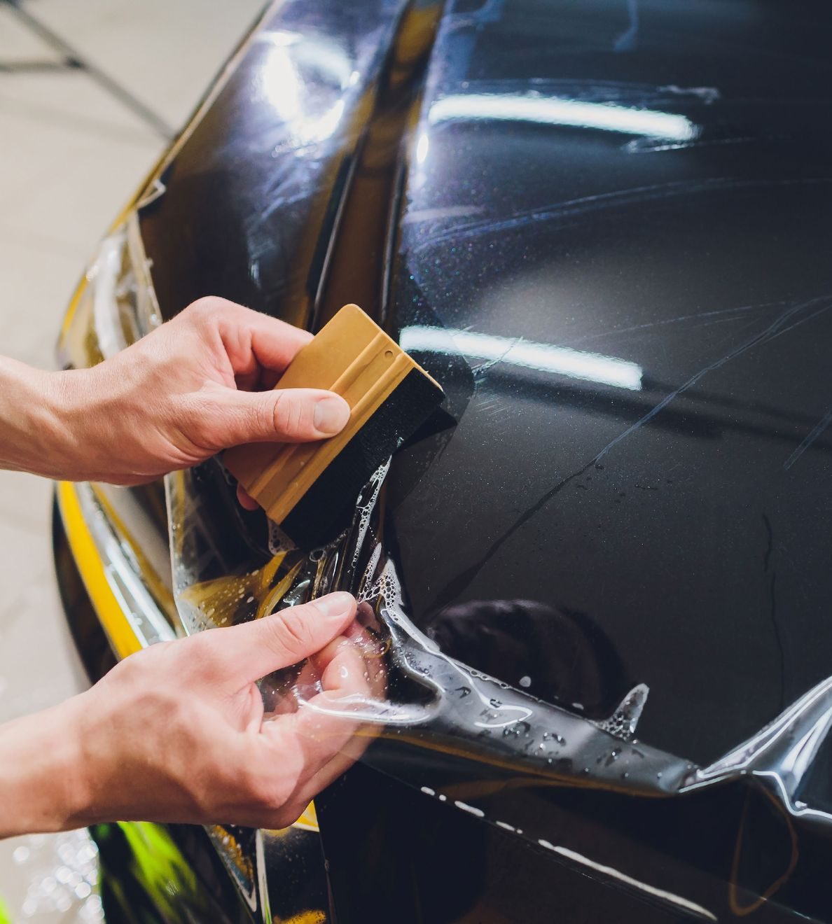 Person with tattoos wiping a black car's surface with a pink cloth in a garage.