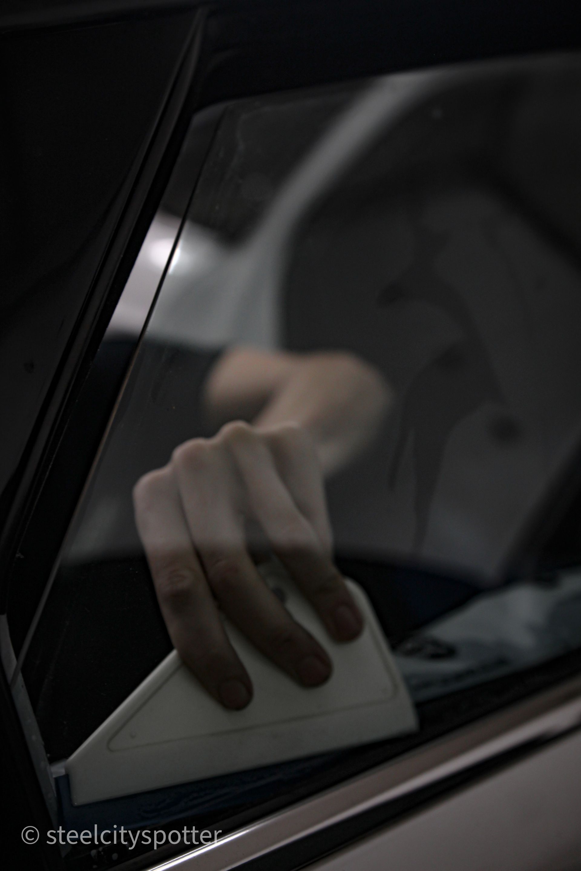 Hand using a squeegee to clean a car window.