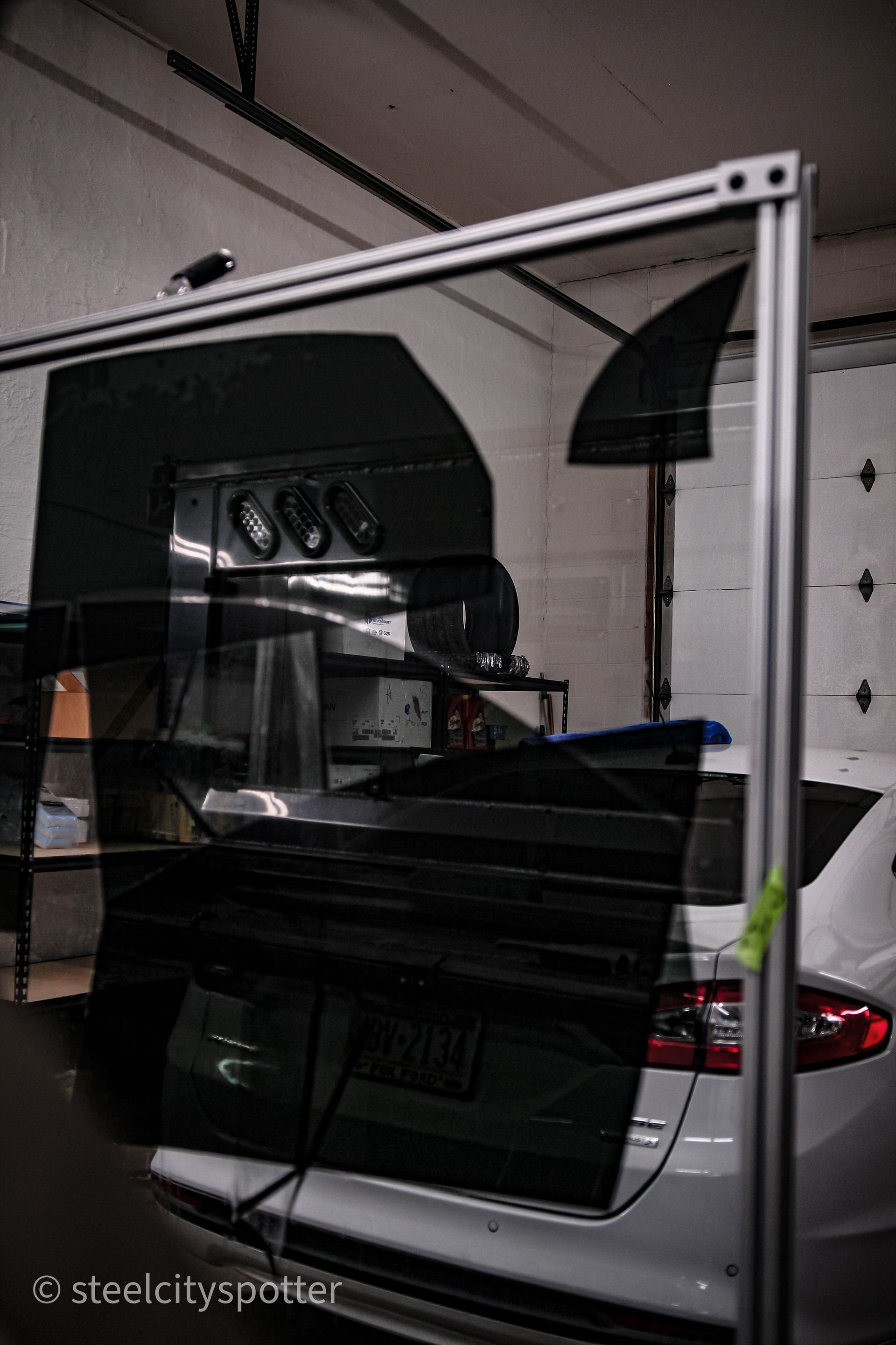 Car with tinted windows, inside a garage with equipment, visible through a framed window tint application.