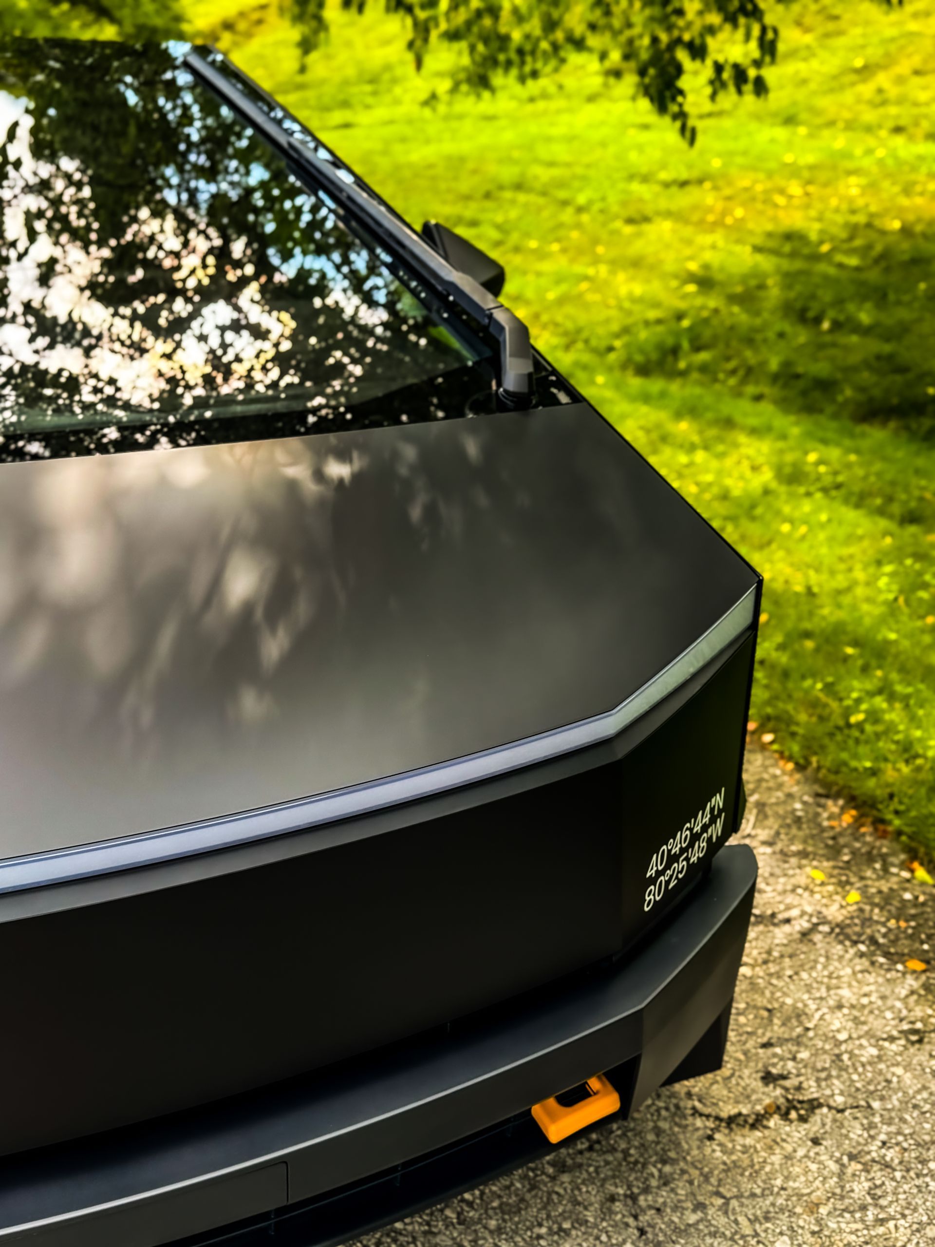 Black Tesla Cybertruck with a matte finish parked on a road, grassy background.