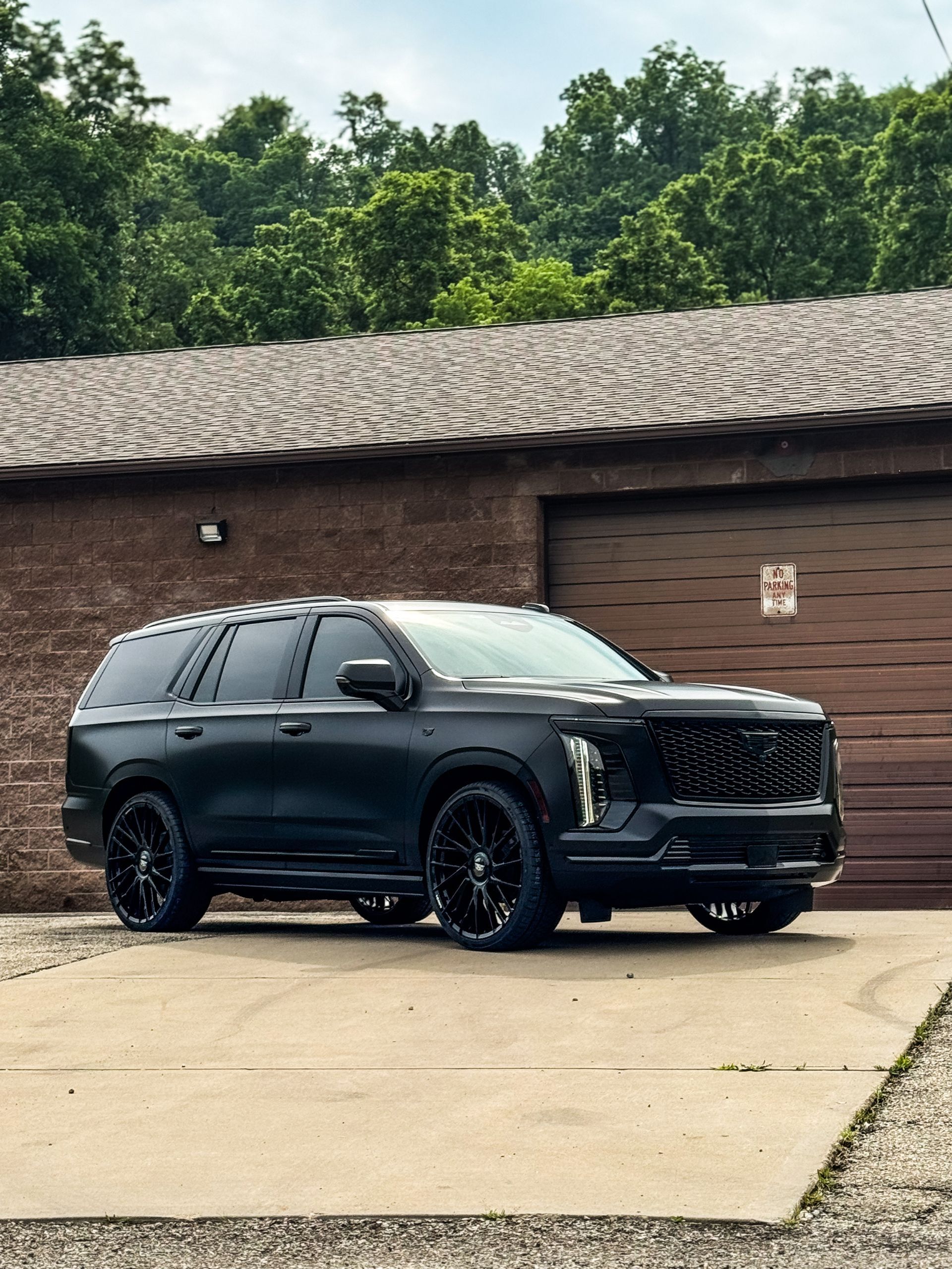 Black Cadillac SUV parked in front of a brick building with a garage door.