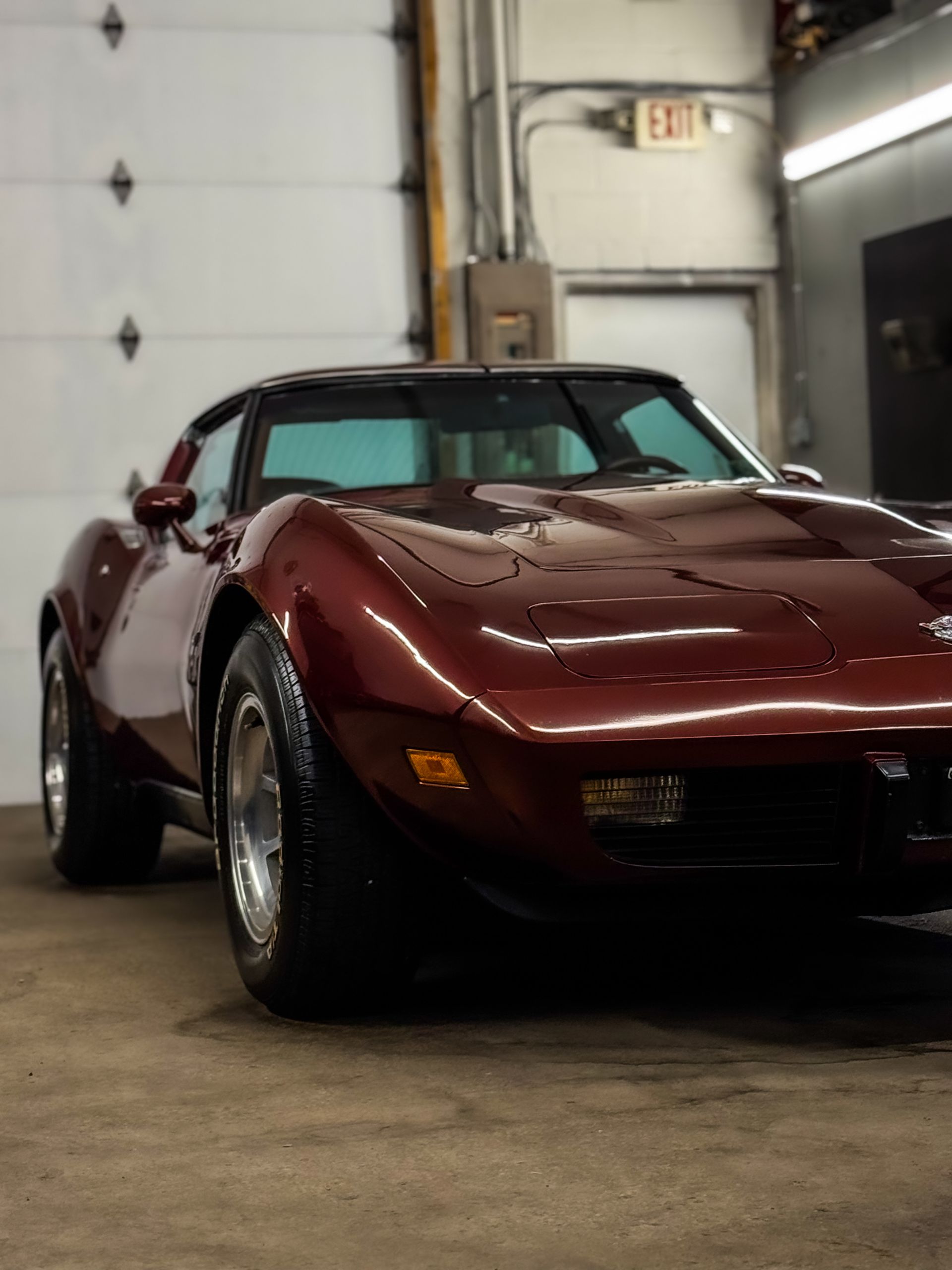Maroon Chevrolet Corvette in a garage with a roll-up door.