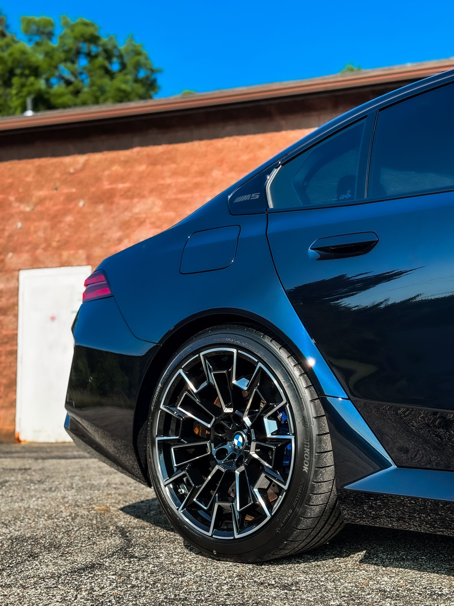 Black BMW car, rear quarter view, with a distinctive wheel design, parked near a brick wall.