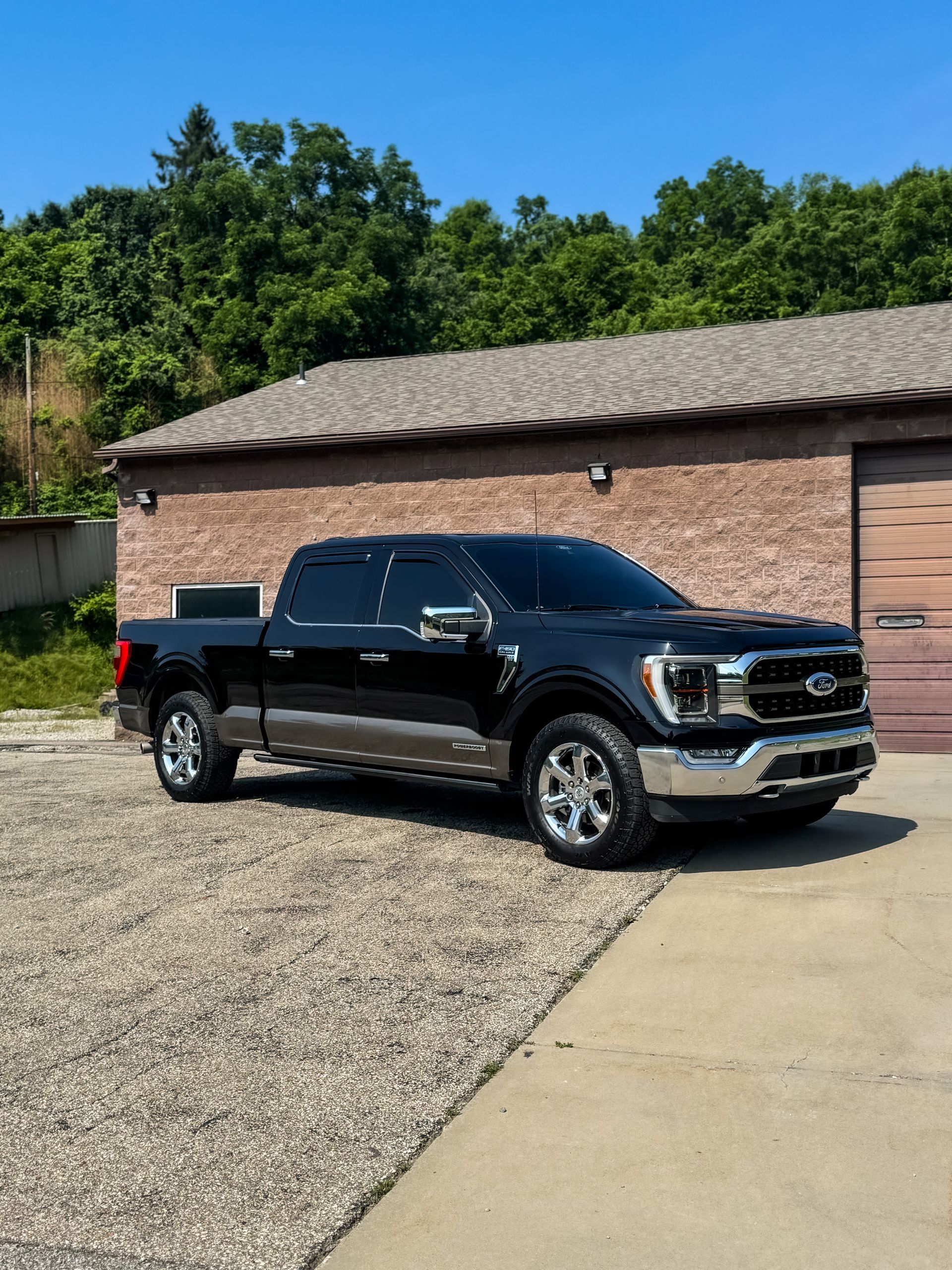 Black and brown Ford truck parked in front of a brick building on a sunny day.