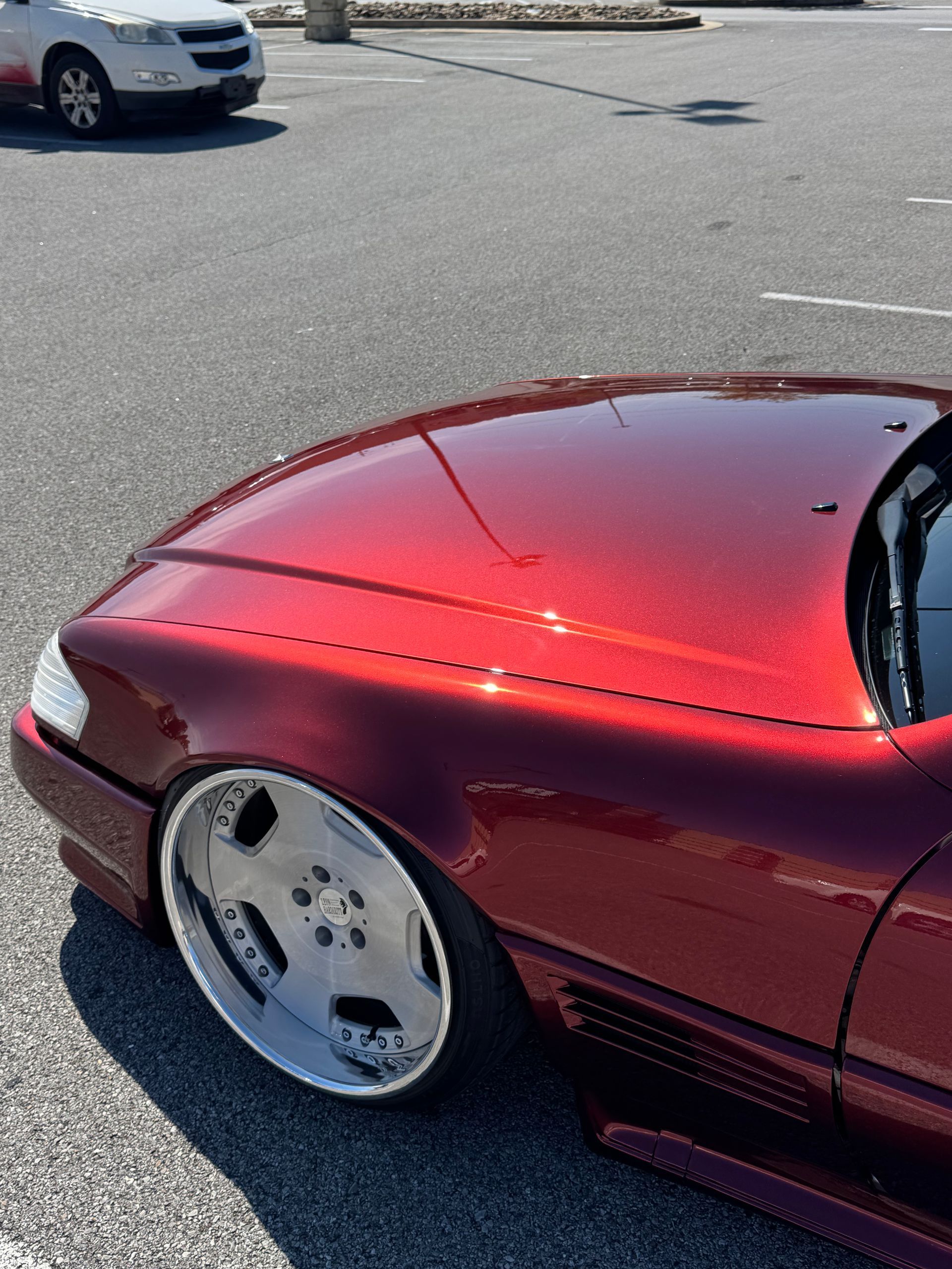Red car with chrome wheels parked on asphalt.