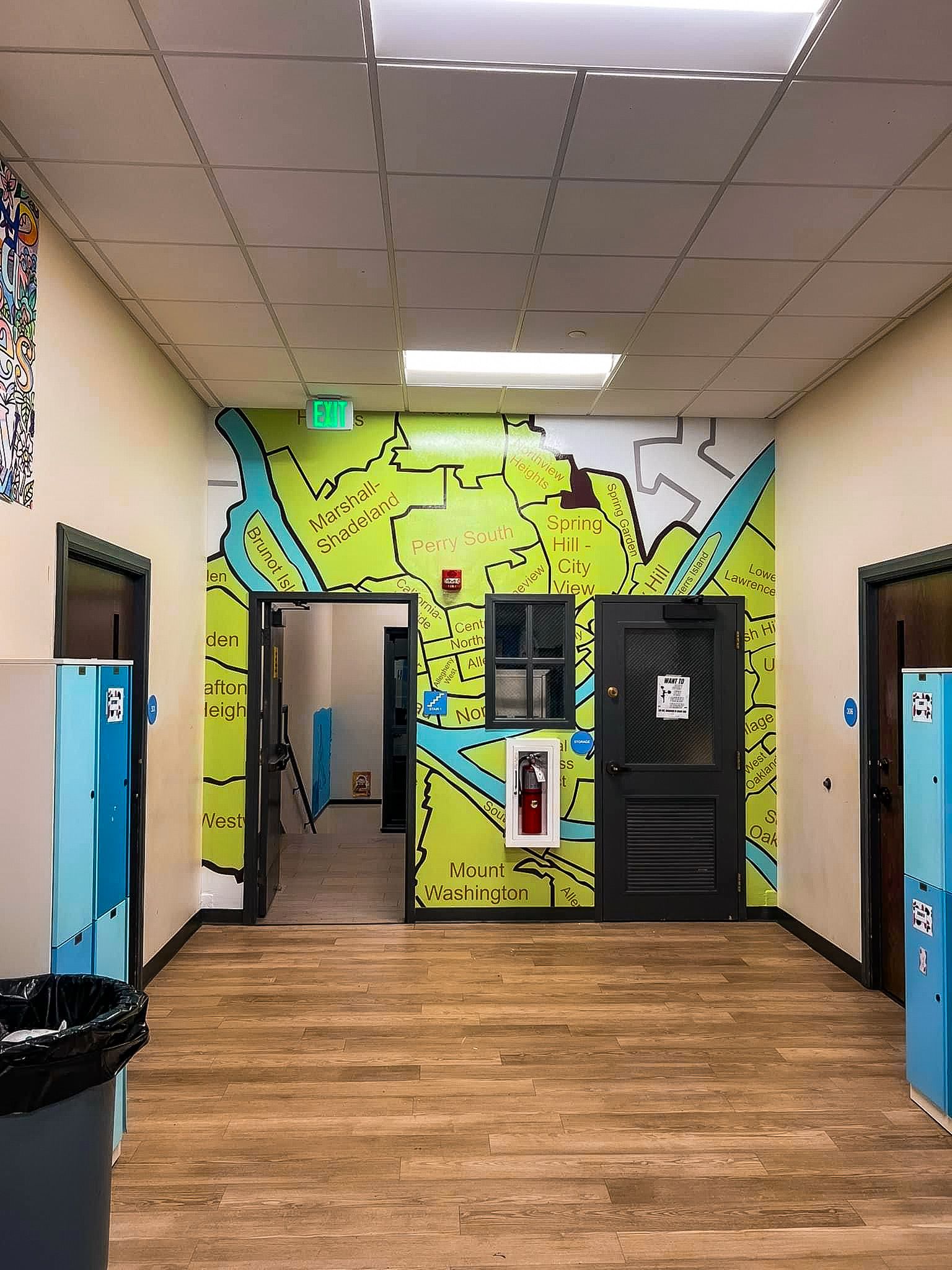 Hallway with a green and teal mural, wooden floor, and black doors.