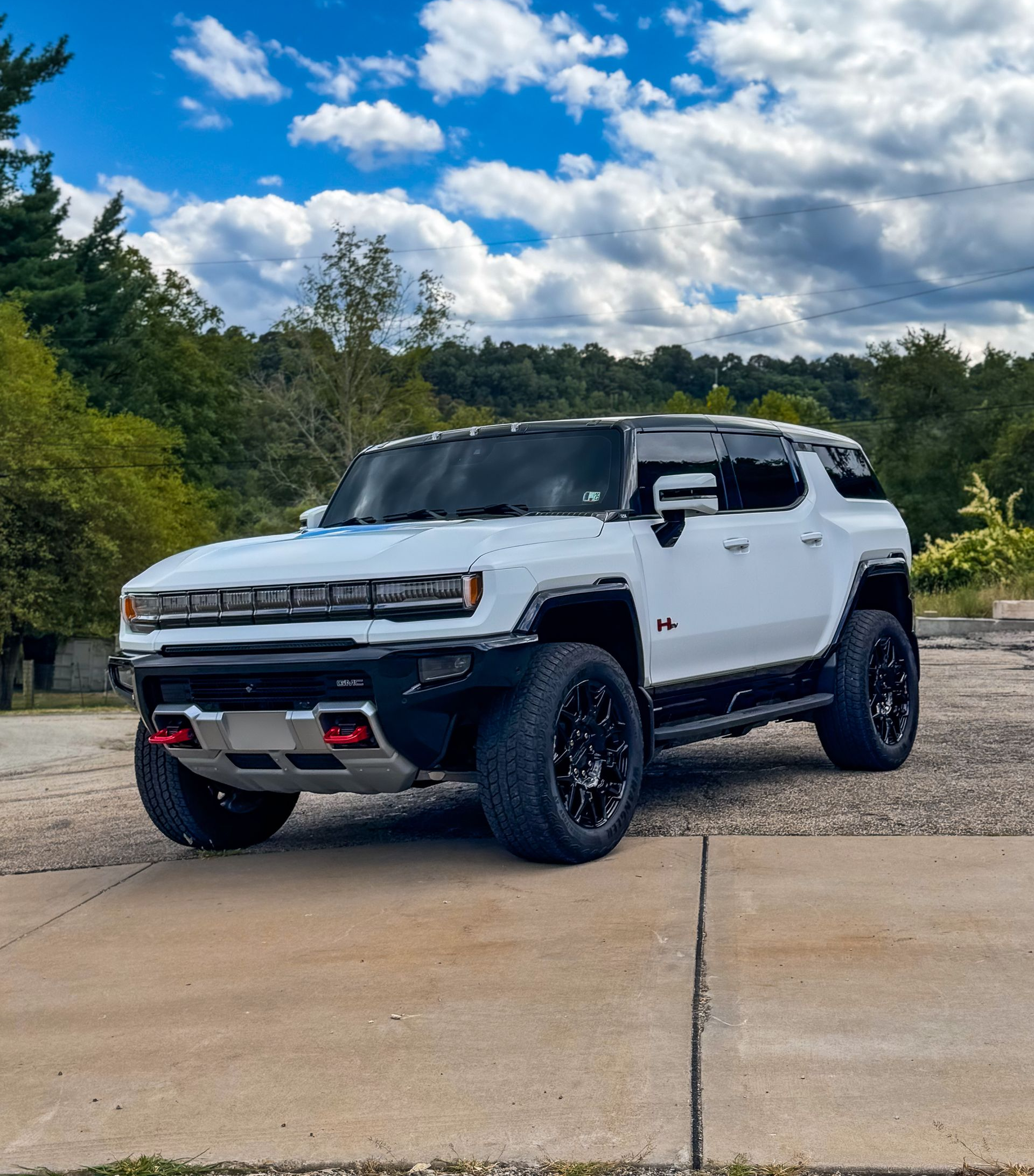 White Hummer EV SUV parked on concrete against a cloudy blue sky and trees.
