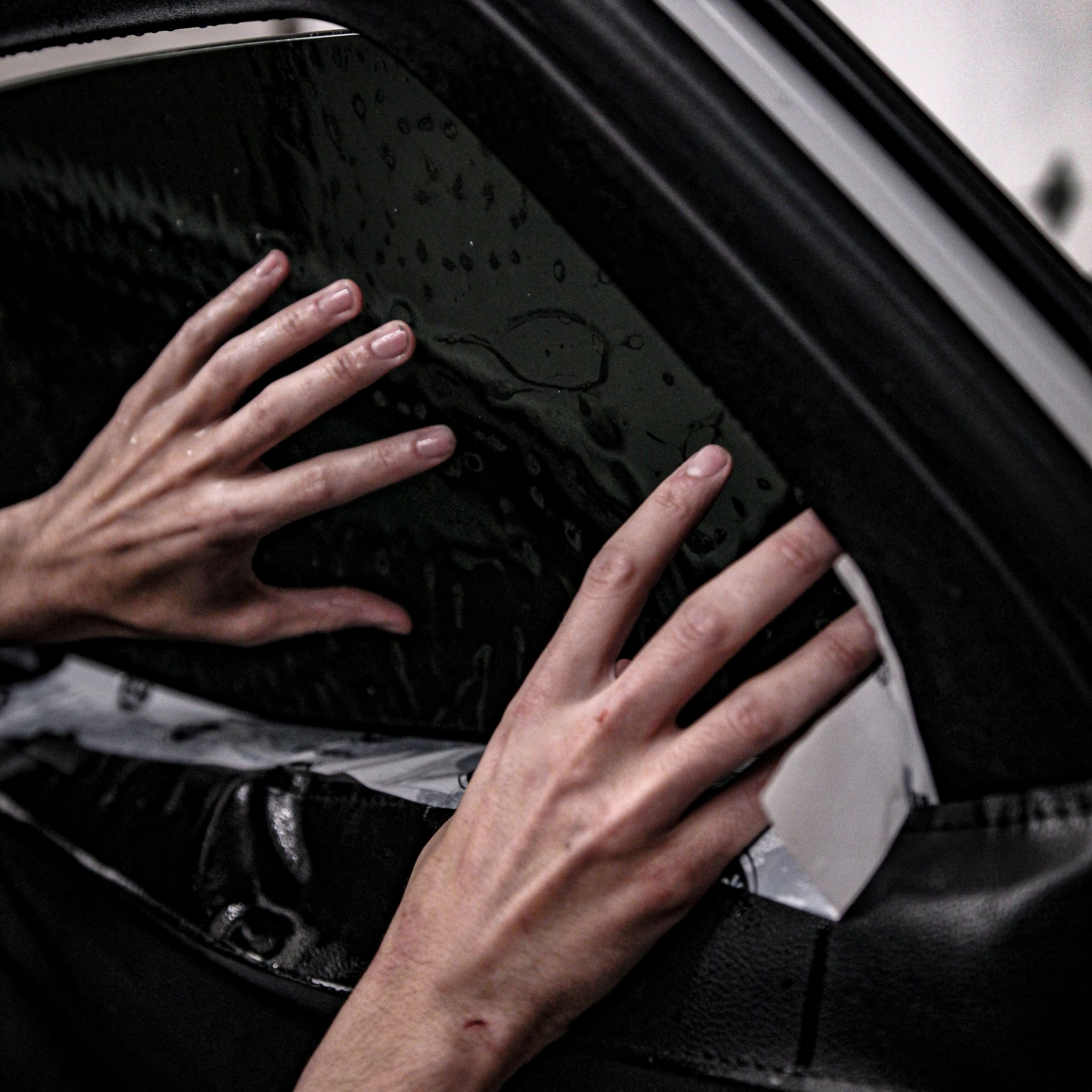 Hands applying tint film to a car window.