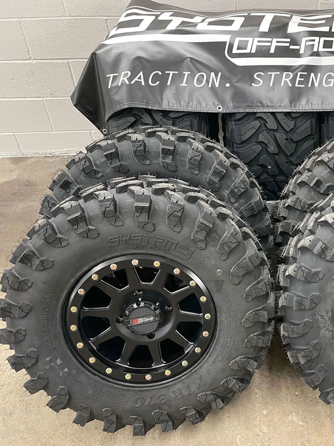 Off-road tires stacked, black rims, with prominent tread. System Off-Road banner in the background.