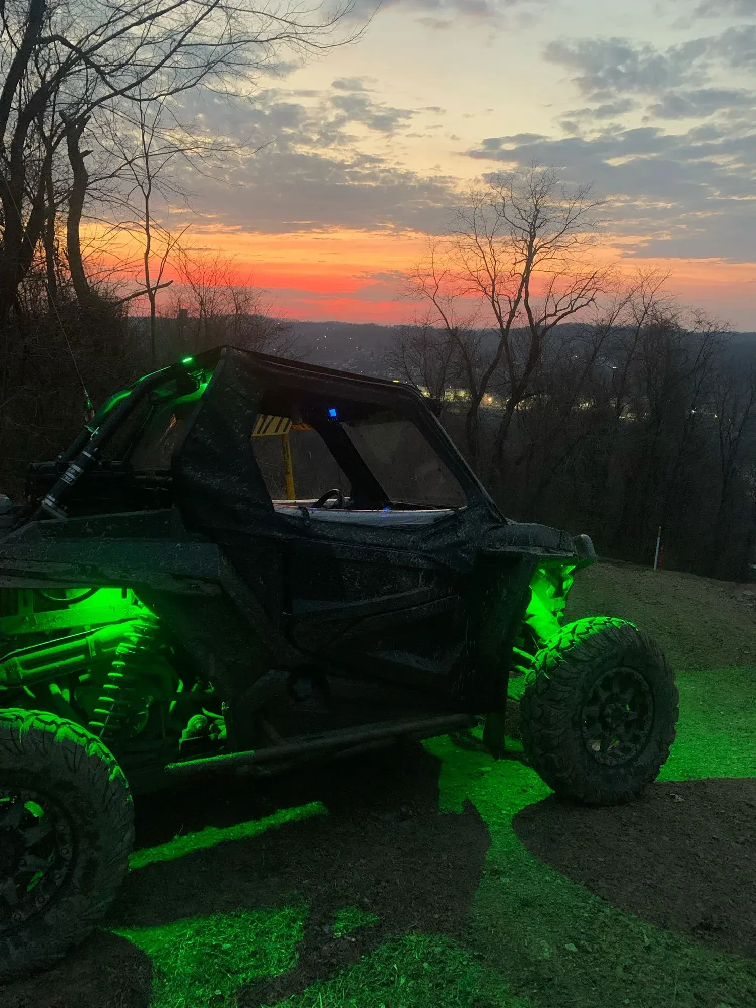 Side-by-side ATV with green underglow lights parked on a hill overlooking a sunset.