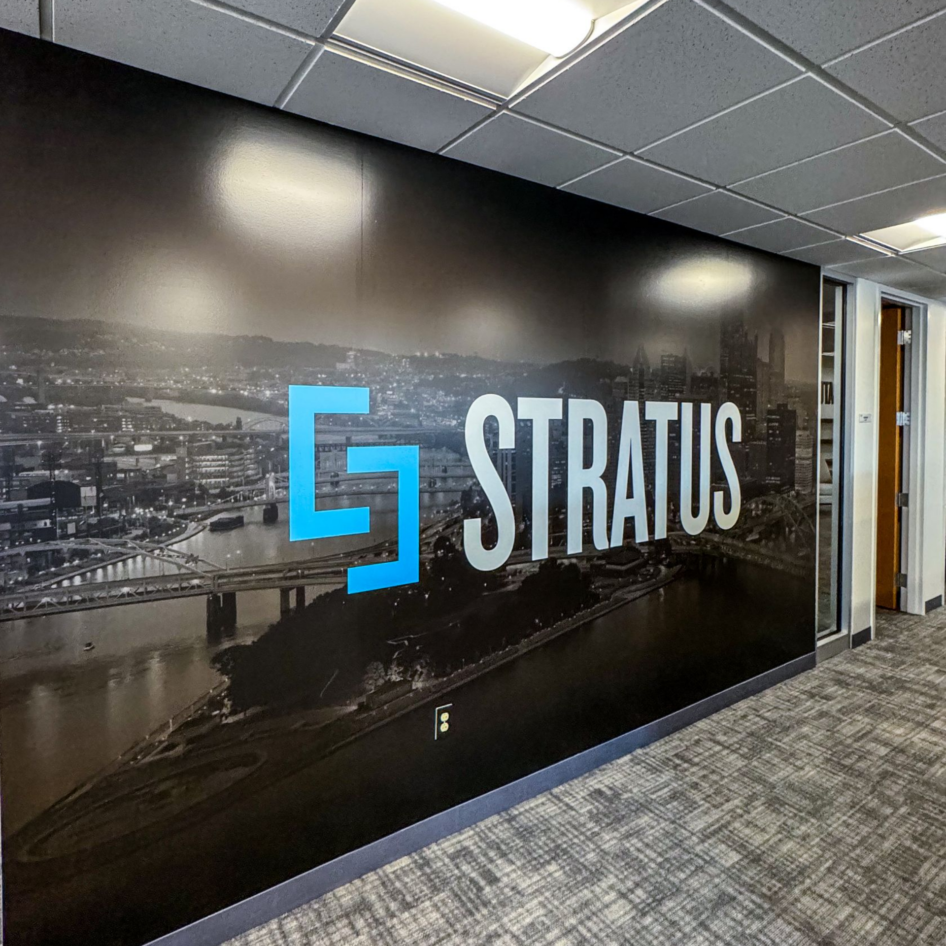 Logo for Stratus in blue and white over a city skyline on a large office wall.