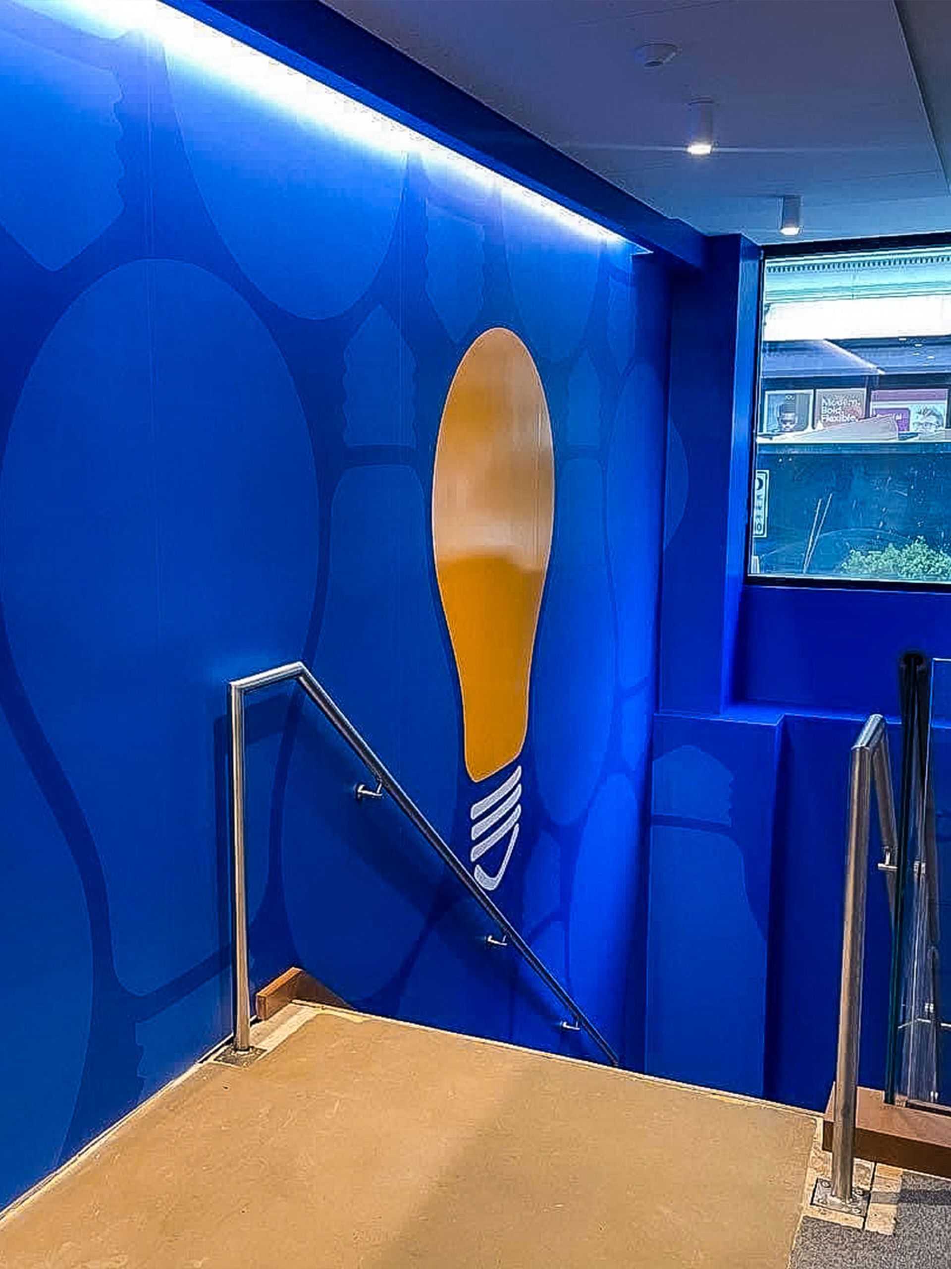 Blue-walled area with a large lightbulb graphic. Staircase with railing leads down. Window shows aquatic life.