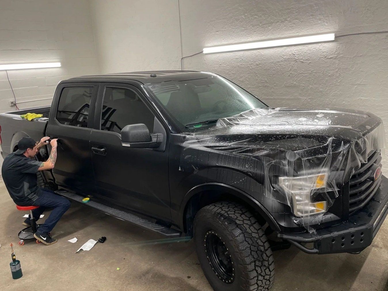 A person applies protective film to a black truck in a garage.