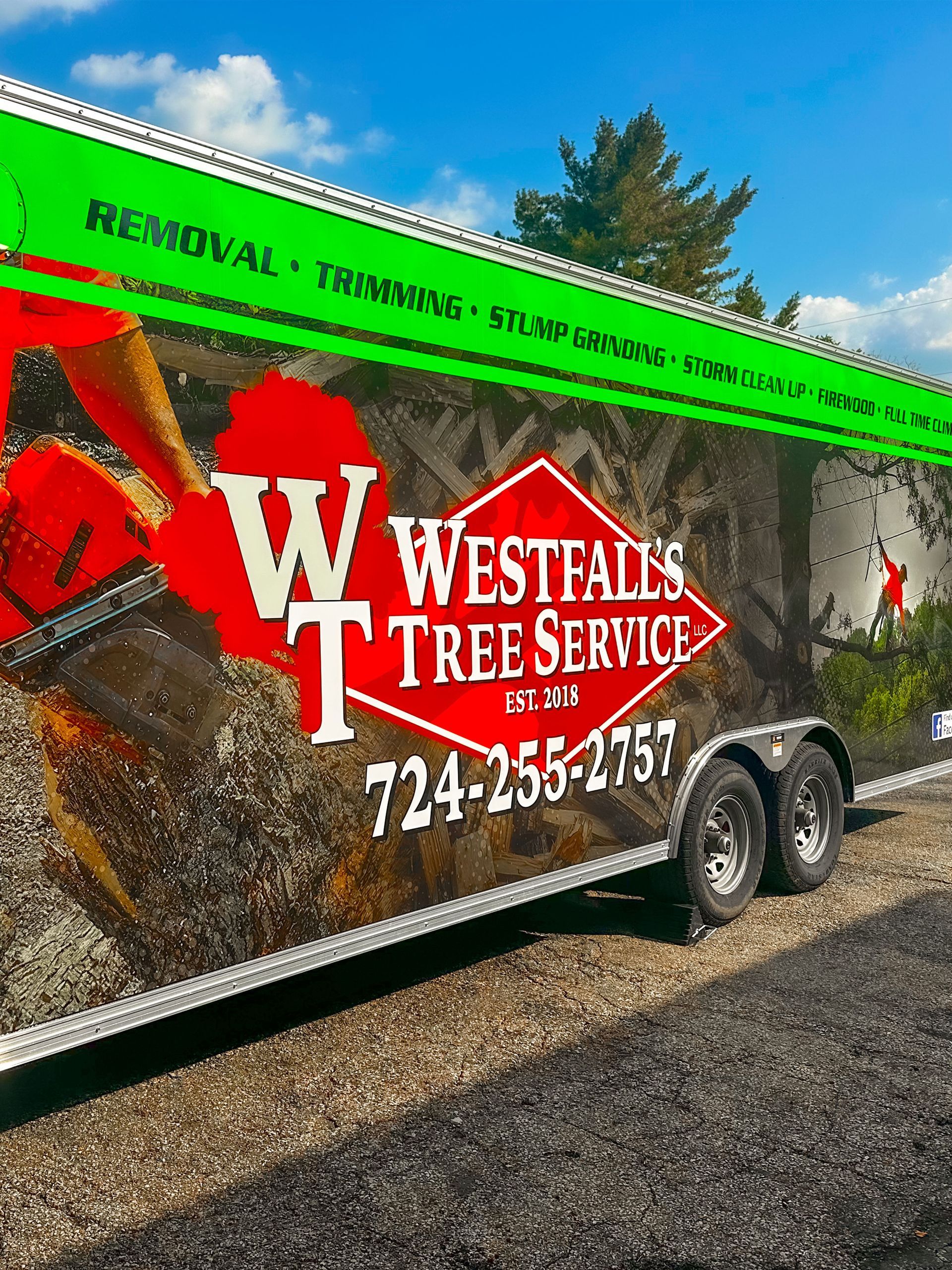 Westfall's Tree Service trailer with logo and phone number, against a blue sky.