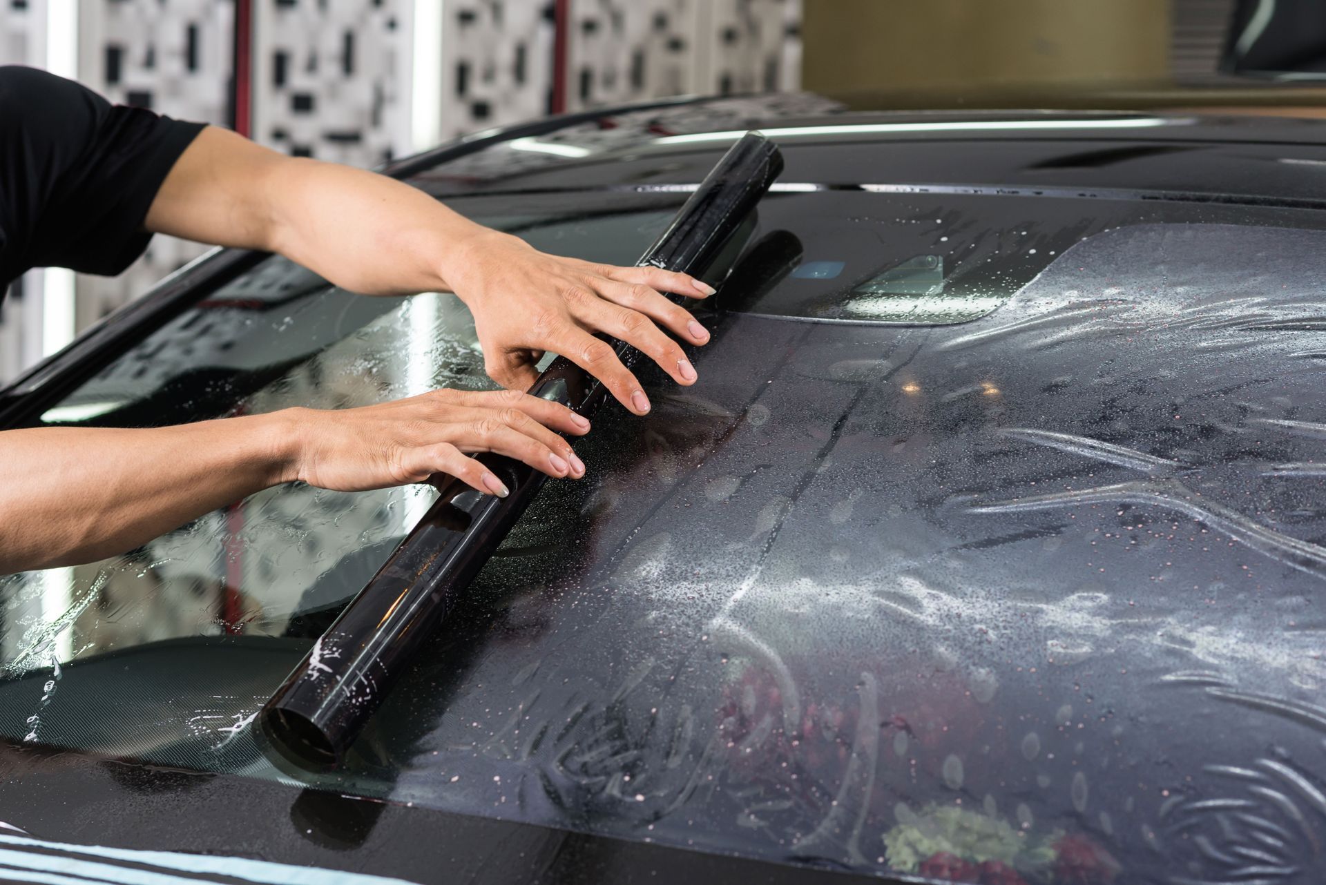 Person applying film to a car's windshield with a squeegee.