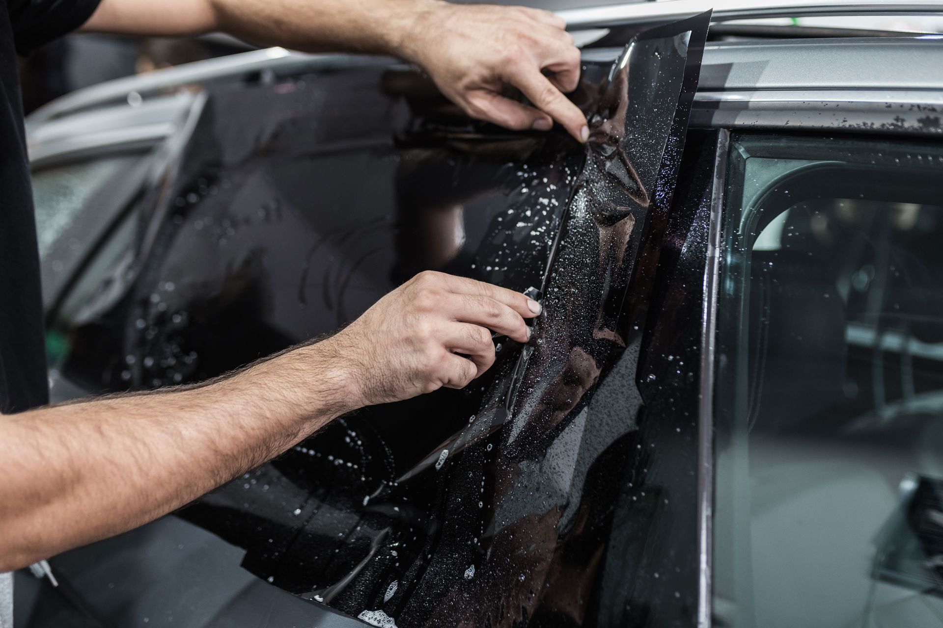 Hands applying dark window tint to a car window.