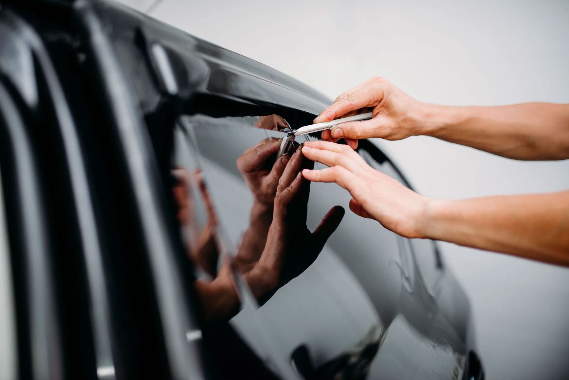 Person using a utility knife to trim car window tinting film. Dark car, light setting.