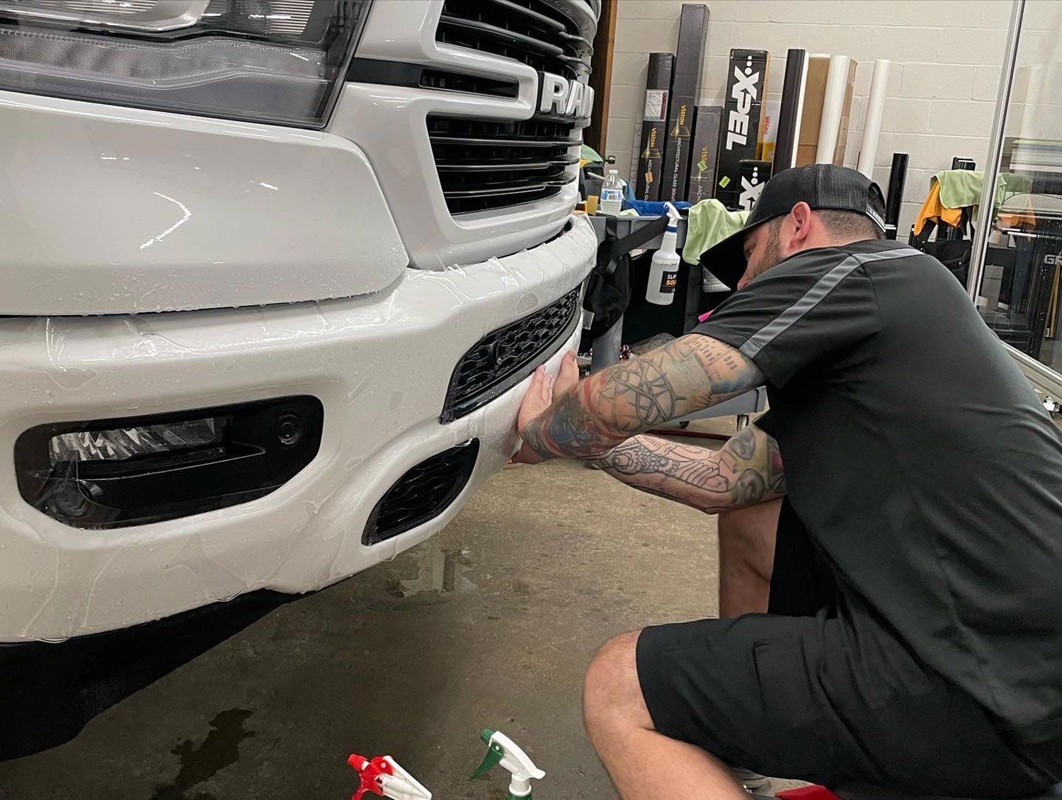 Person applying protective film to the bumper of a white truck in a shop.