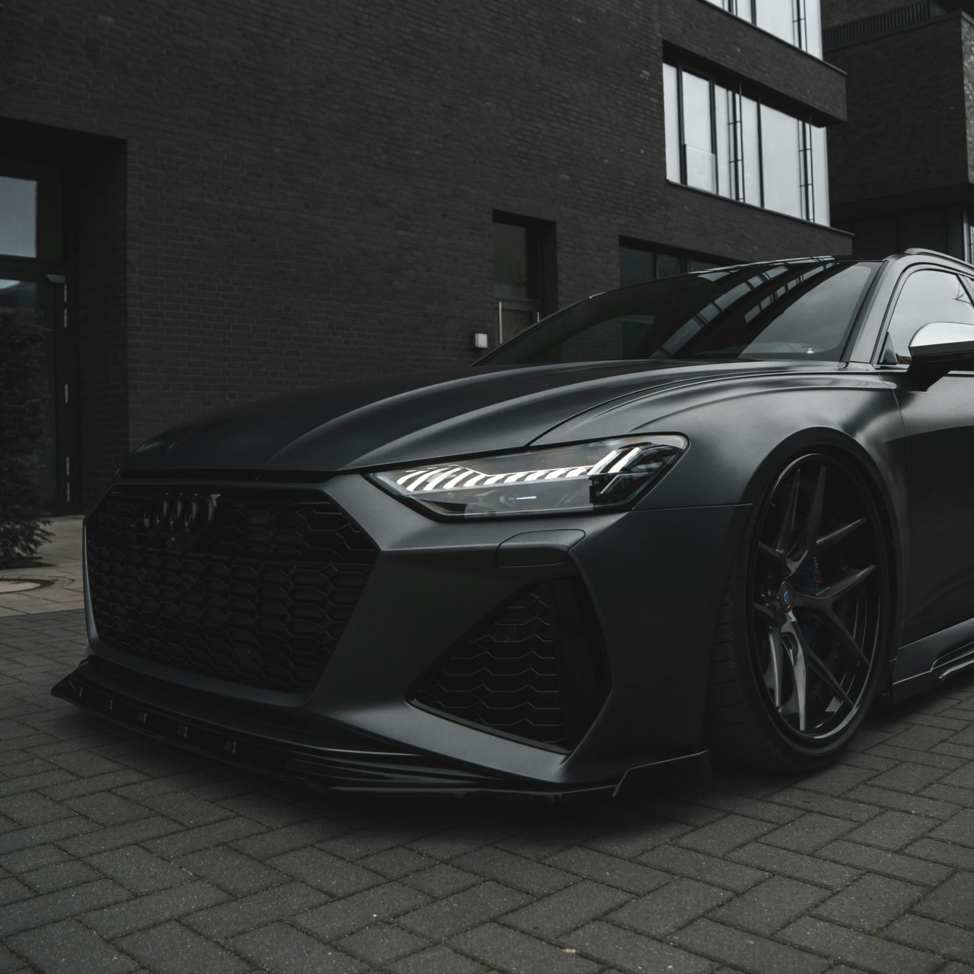 Dark grey Audi RS6 parked in front of a dark brick building.