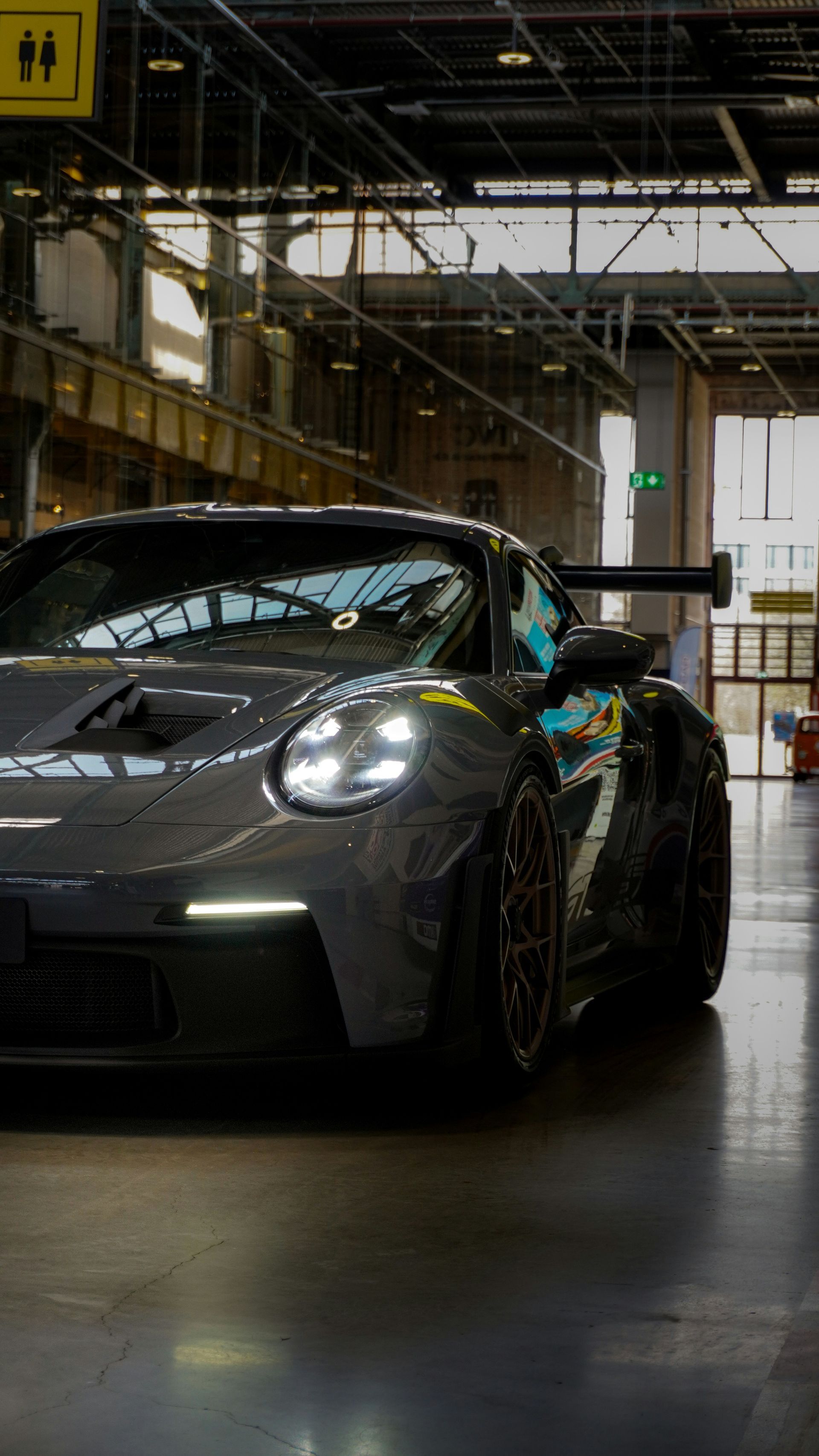 Dark gray Porsche sports car inside a modern building, front view, headlights on.