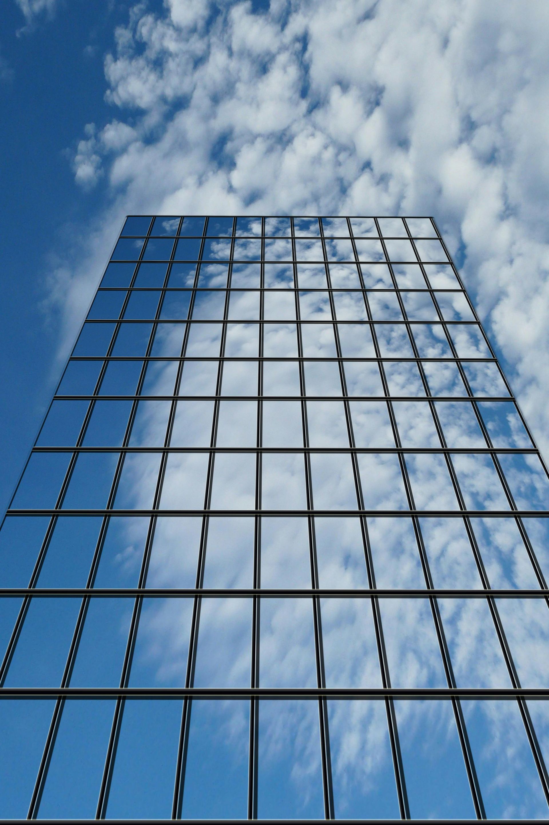 Glass building reflecting blue sky and fluffy white clouds.