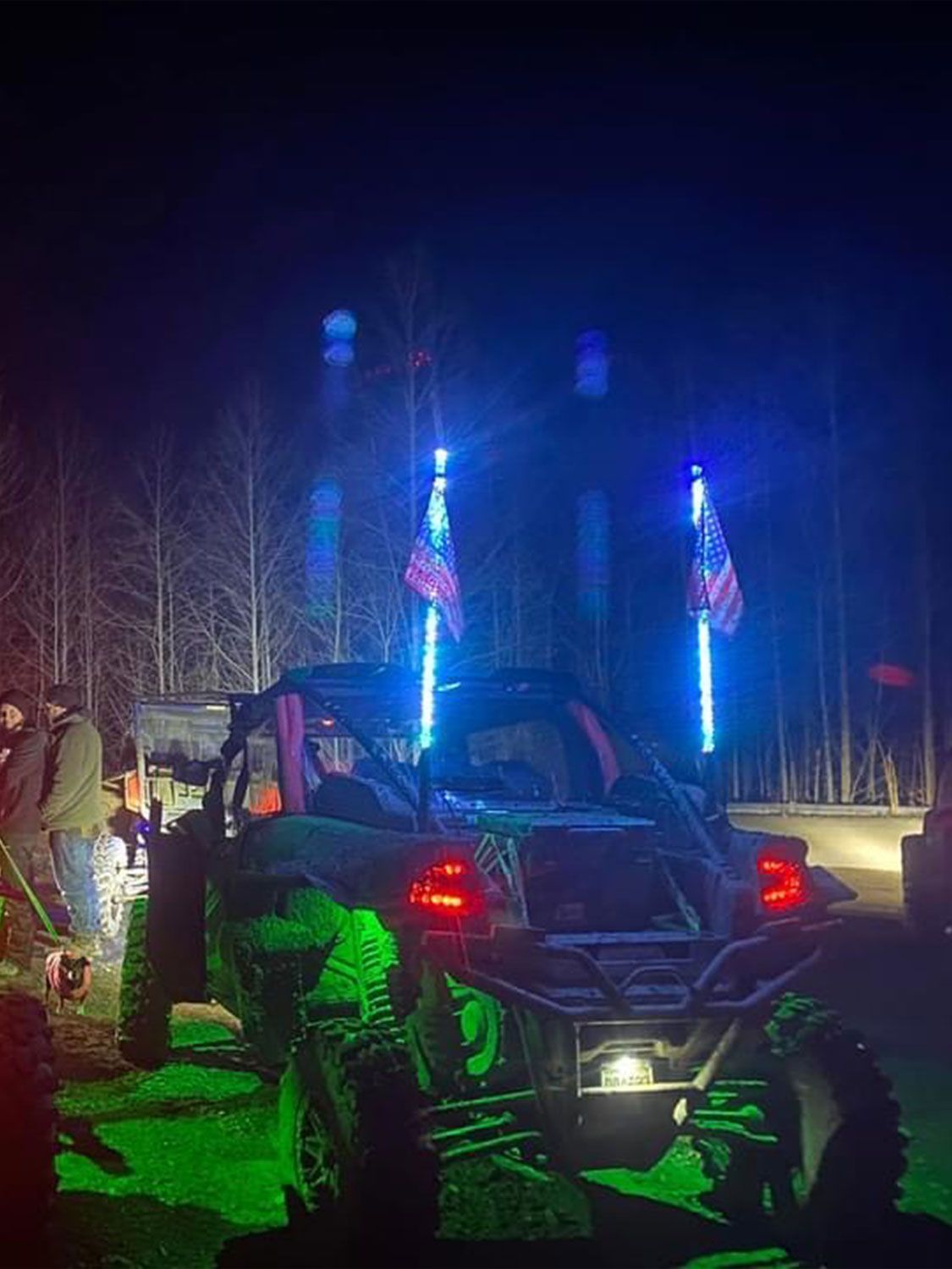 A UTV at night with green and blue lights, with American flags on light poles.
