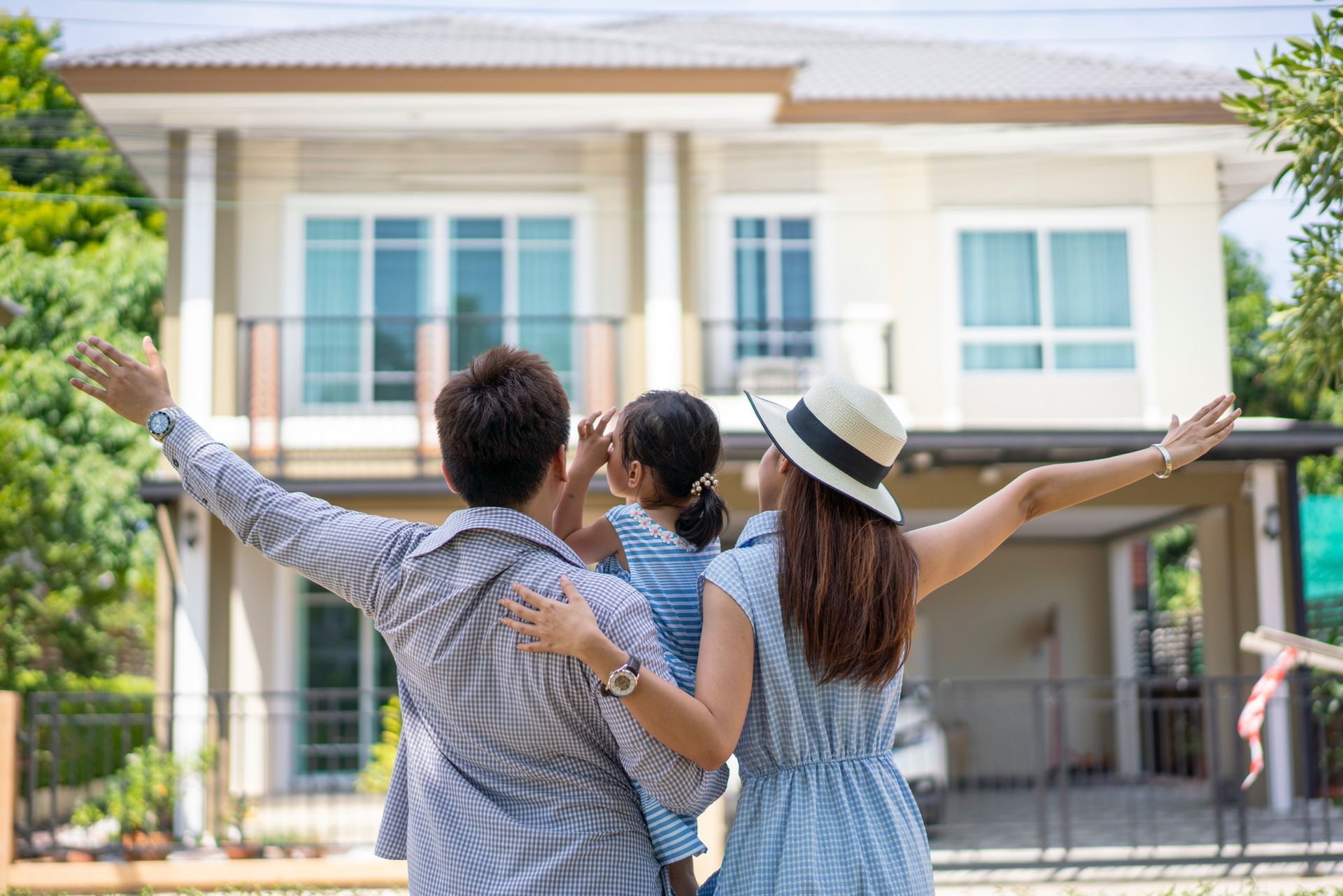 A family is standing in front of a house with their arms outstretched.