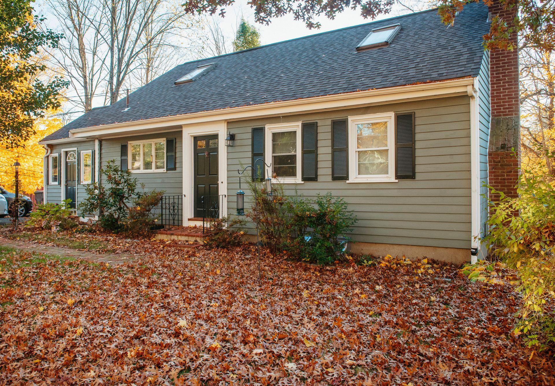 A house with a lot of leaves on the ground in front of it.