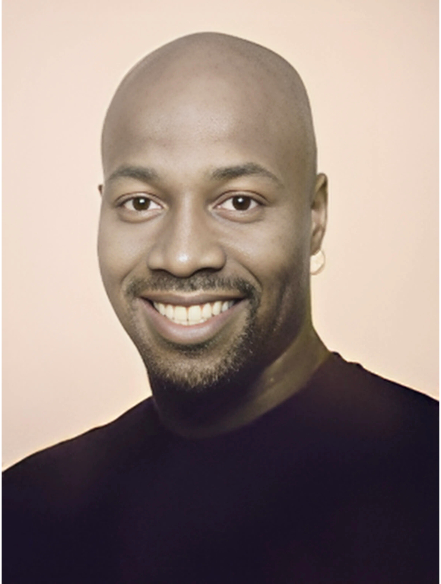 A bald man with a beard is smiling for the camera