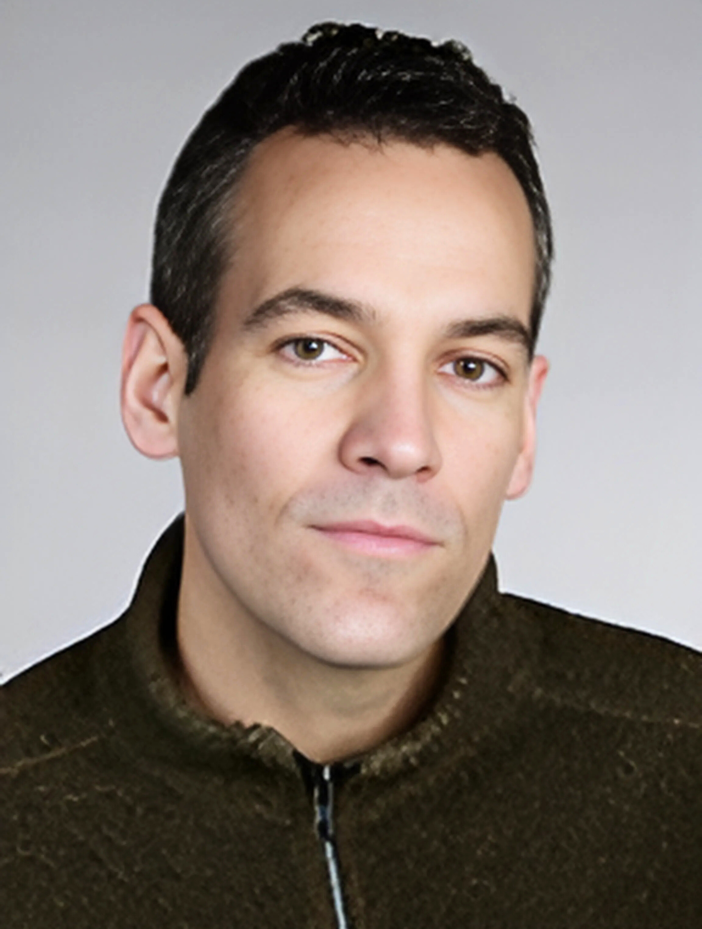 A man wearing a green sweater looks at the camera