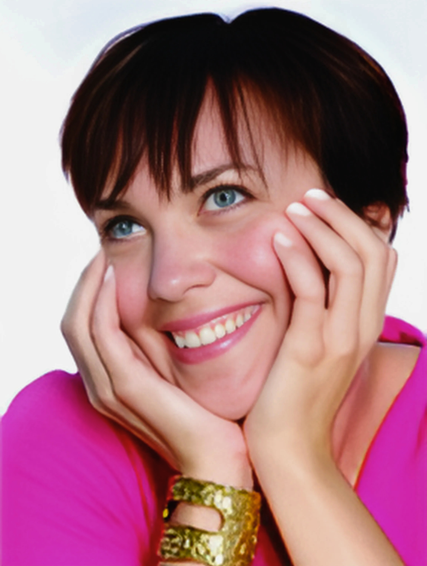 A woman in a pink shirt is smiling with her hands on her face