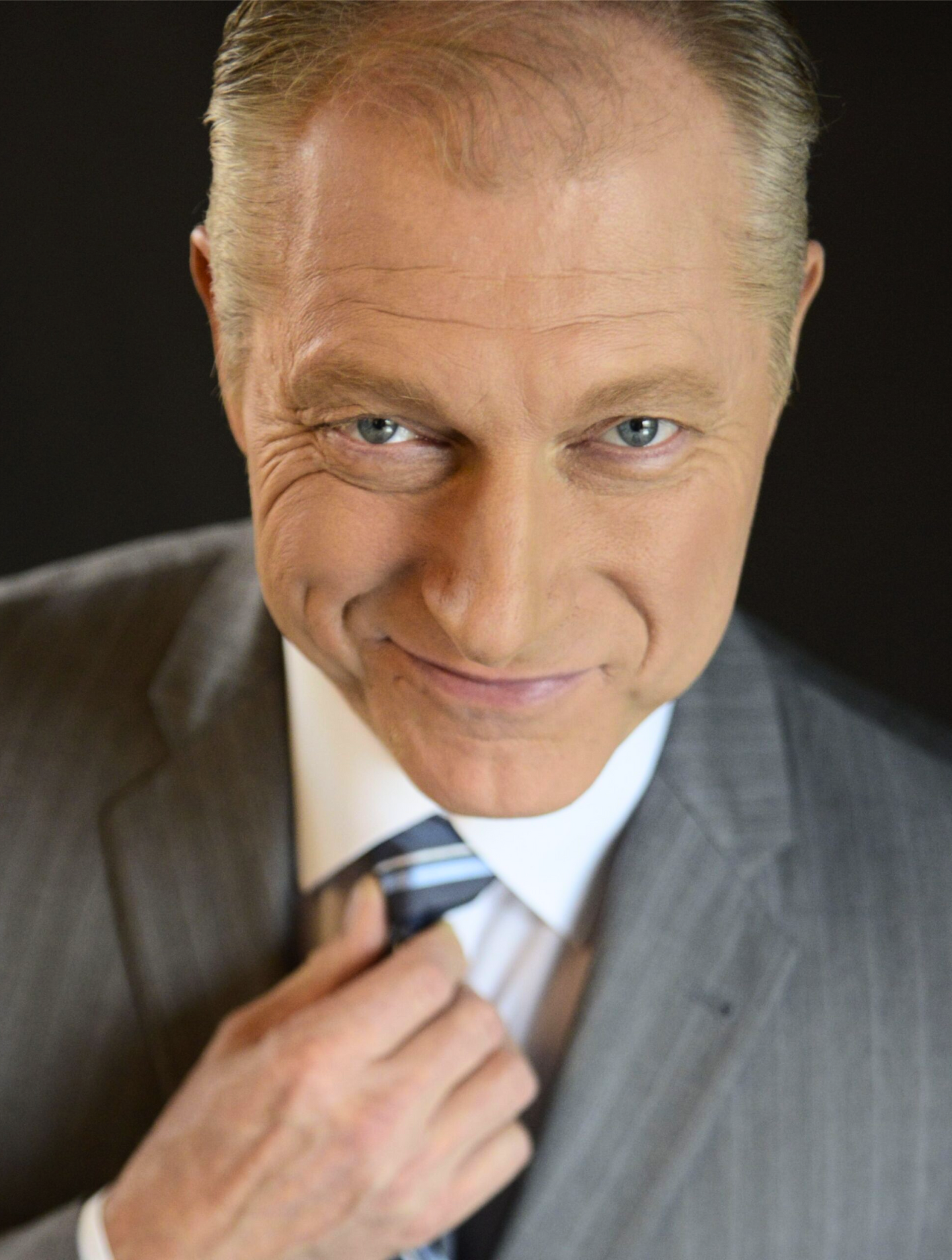 A man in a suit and tie is smiling and adjusting his tie