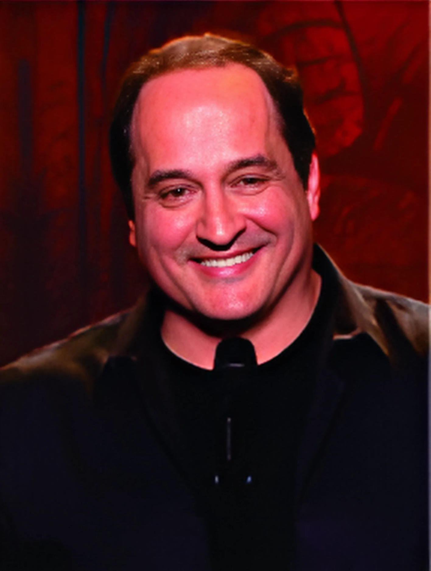 A man is smiling while standing in front of a microphone