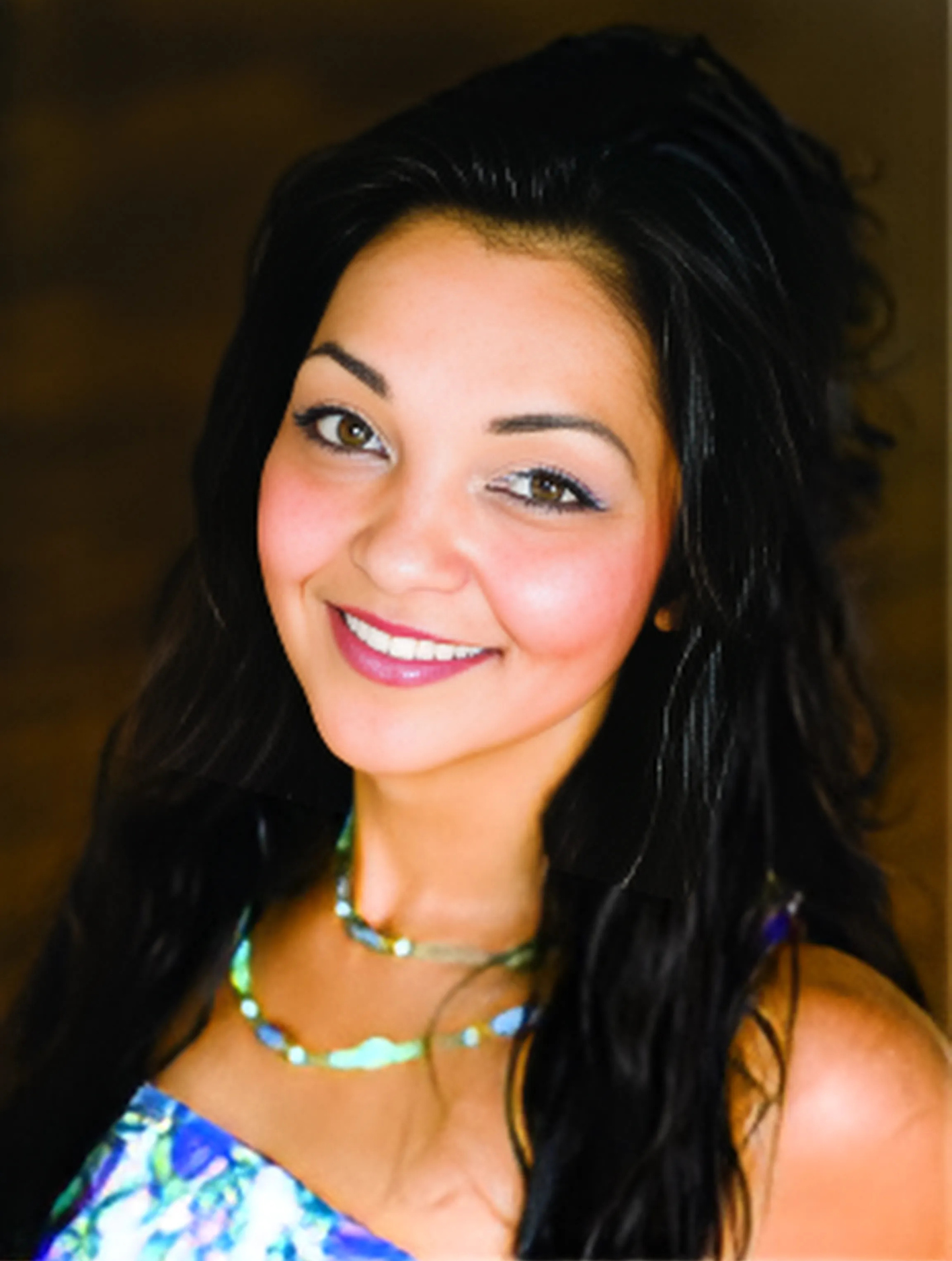 A woman with long hair and a necklace smiles for the camera