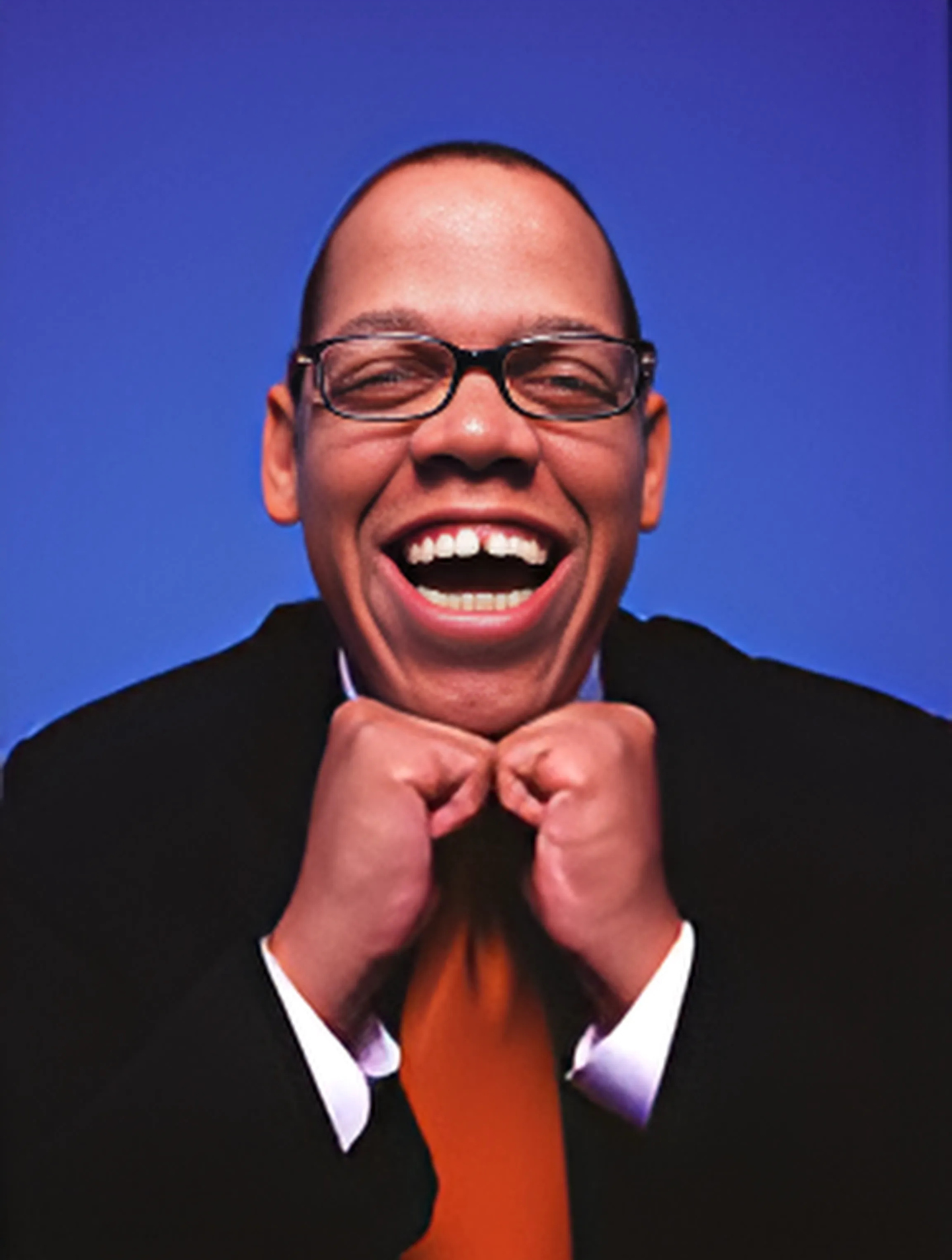 A man wearing glasses and an orange tie is laughing