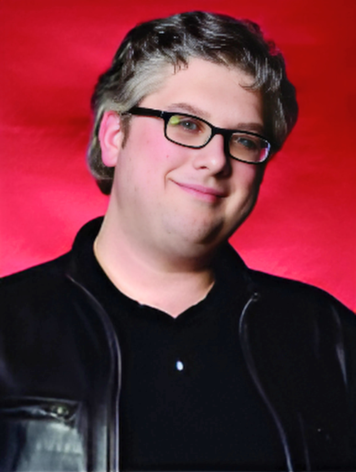 A man wearing glasses and a black jacket smiles for the camera