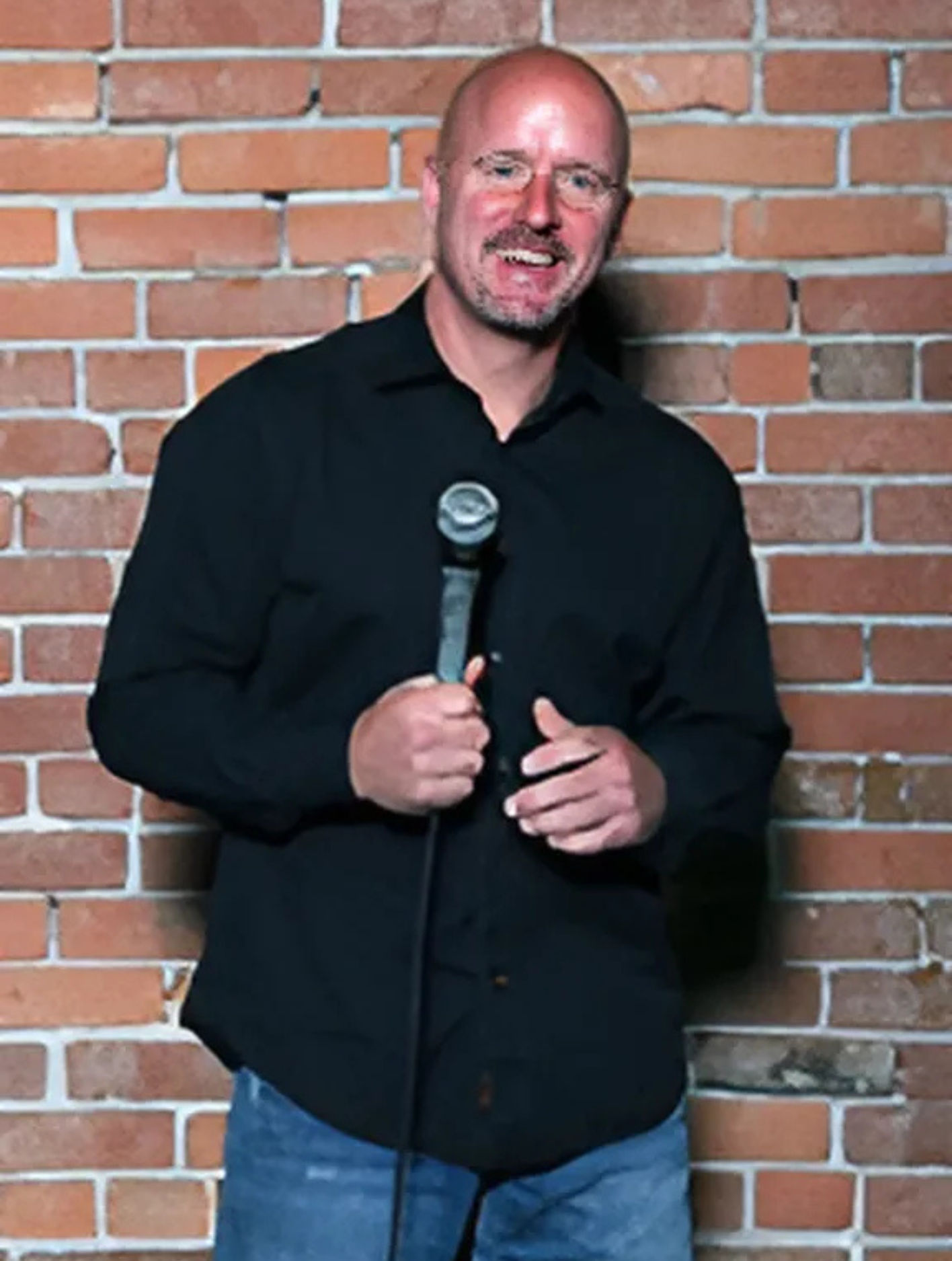 A man in a black shirt is holding a microphone in front of a brick wall