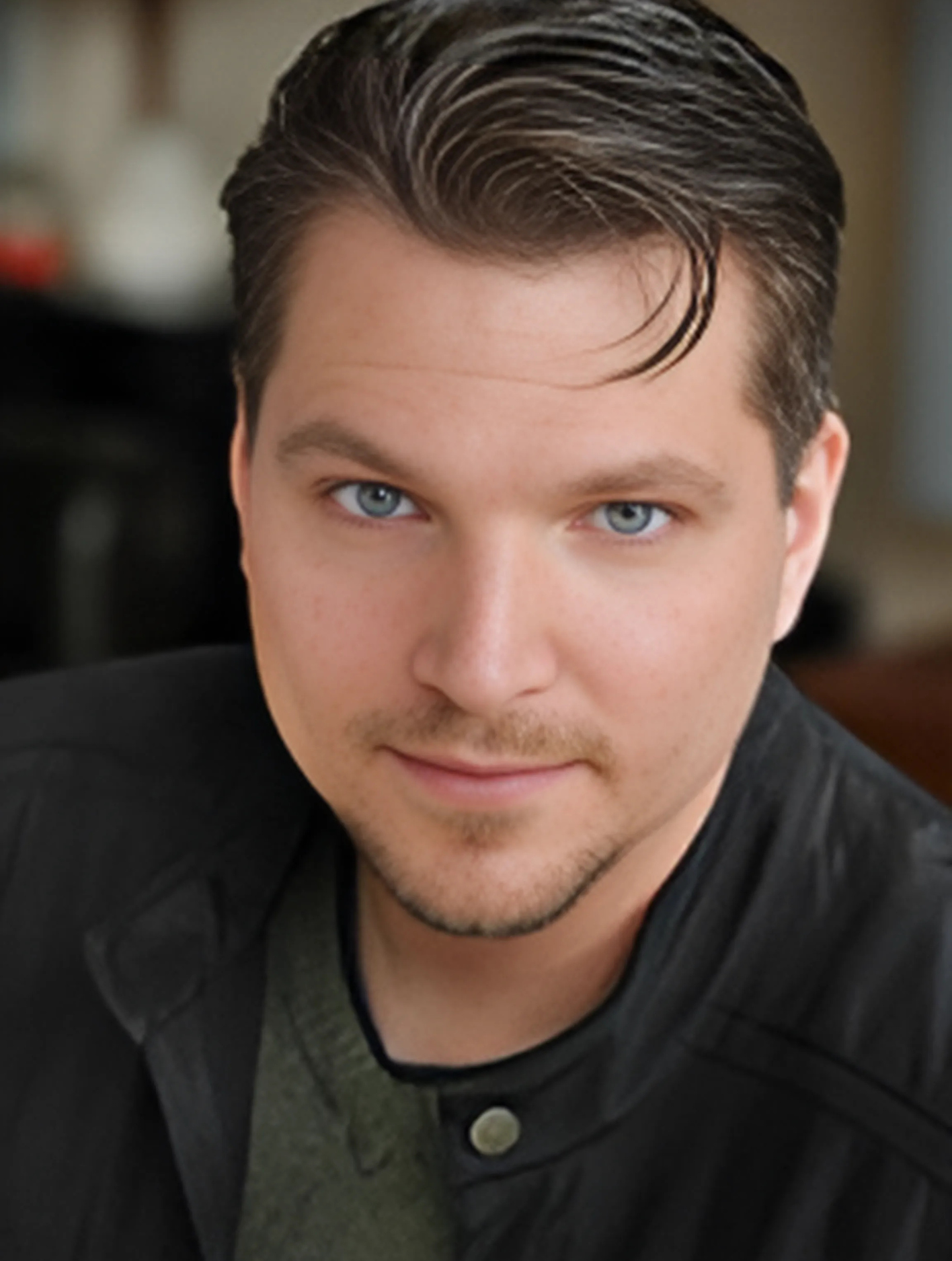 A man with a beard and blue eyes is wearing a black jacket