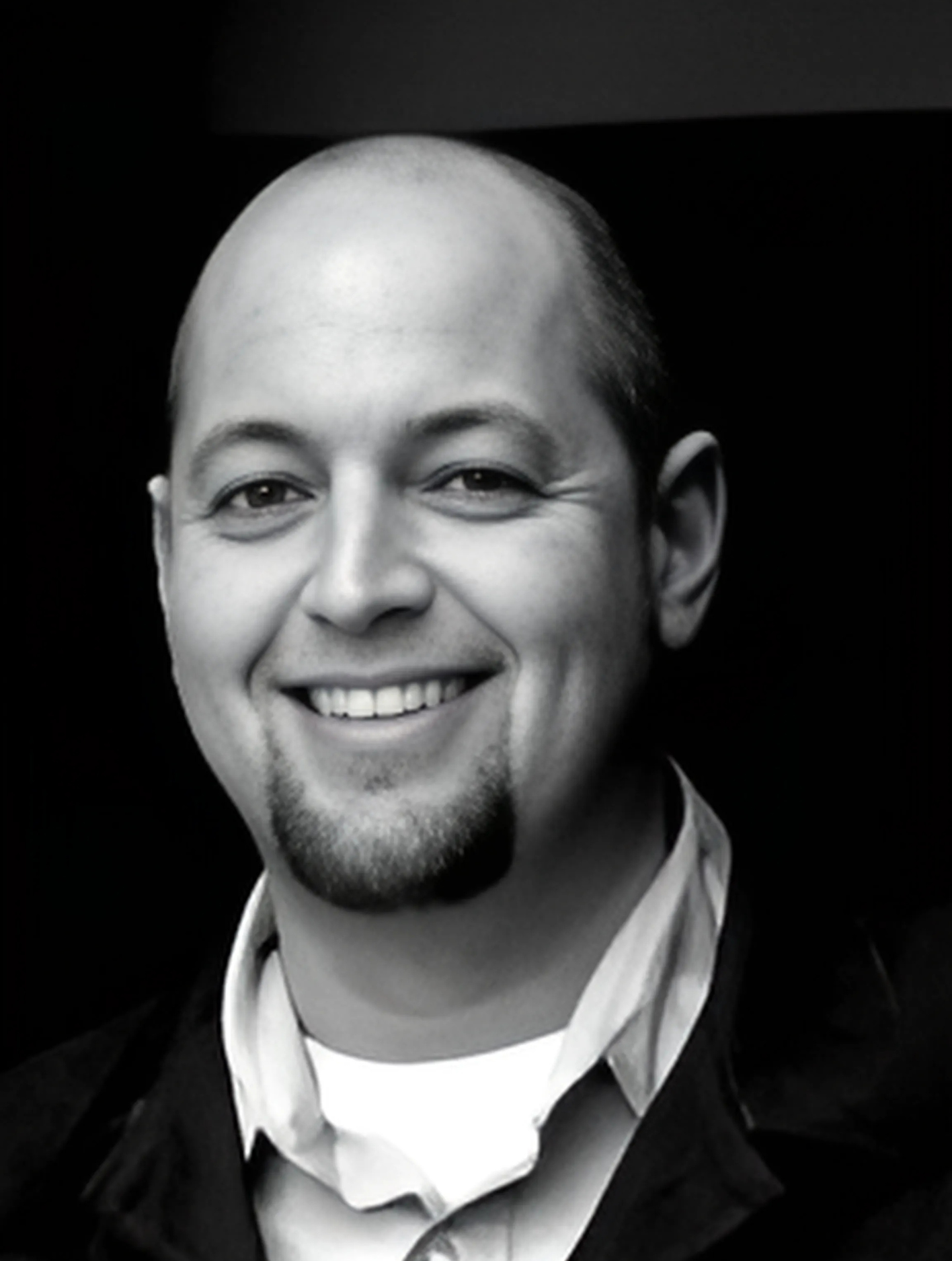 A bald man with a beard is smiling in a black and white photo
