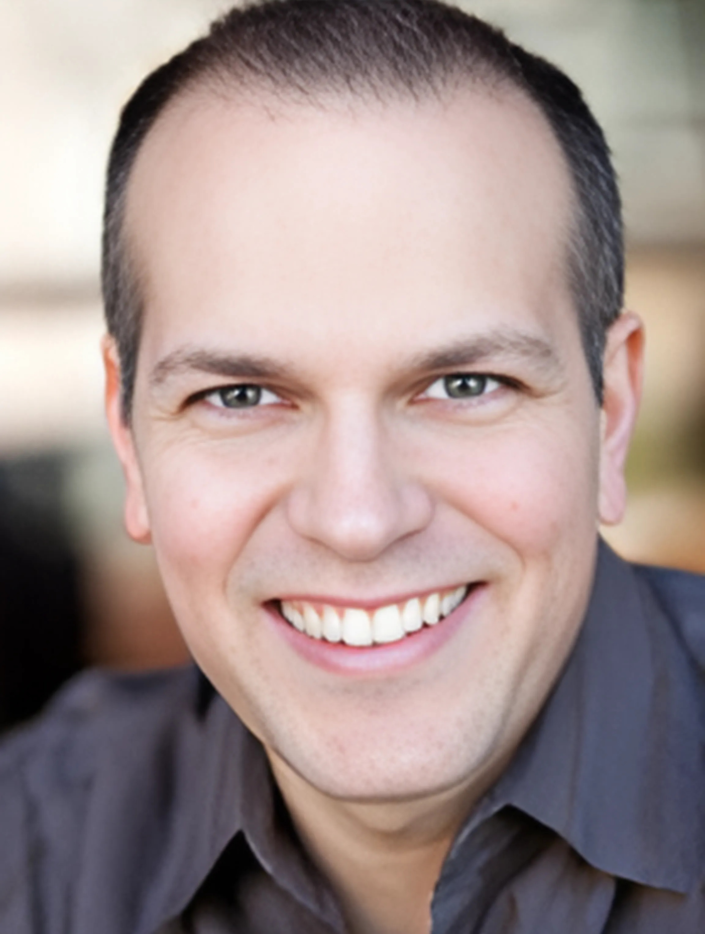 A man in a grey shirt is smiling for the camera