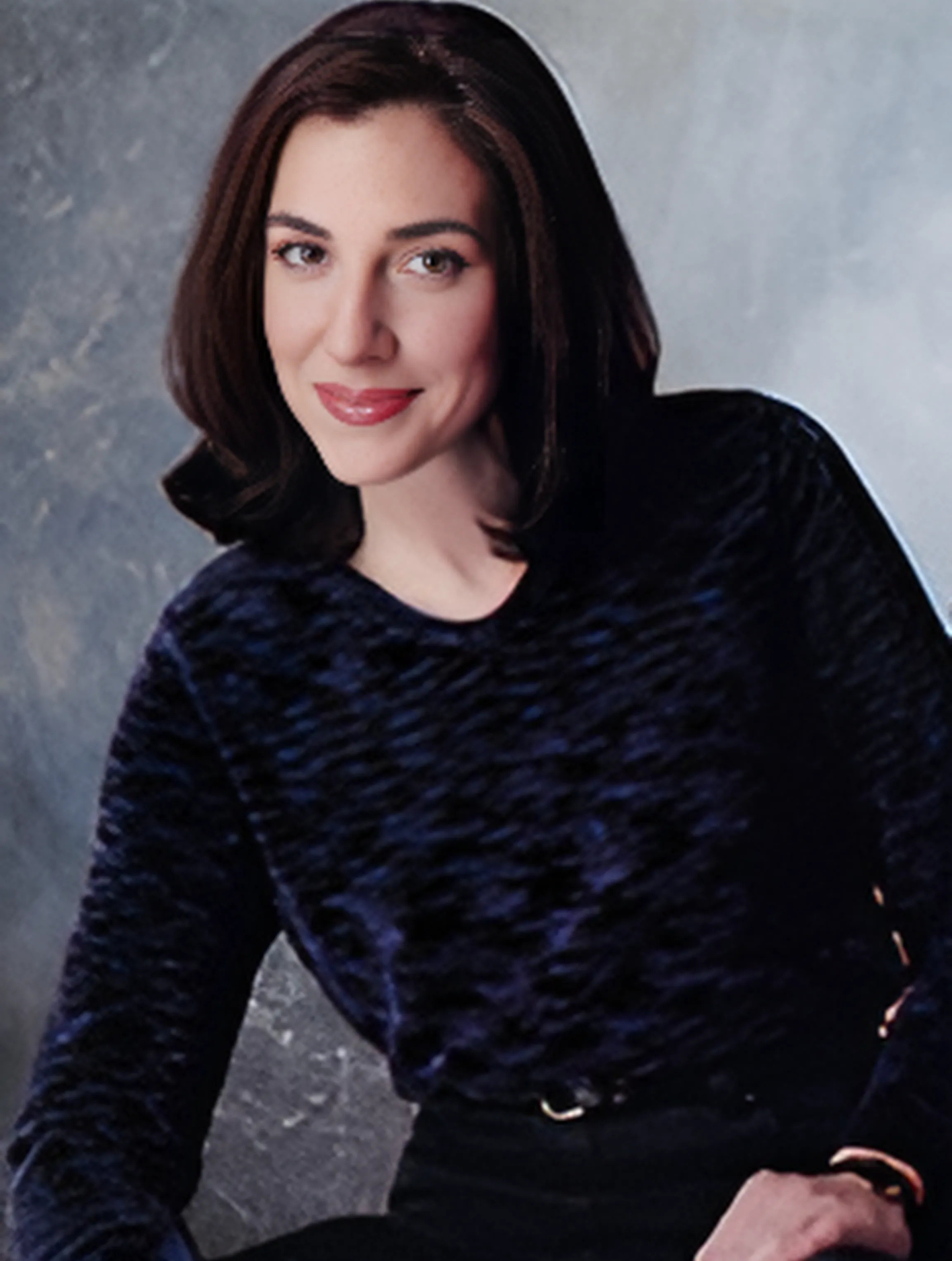 A woman wearing a blue sweater and black pants smiles for the camera