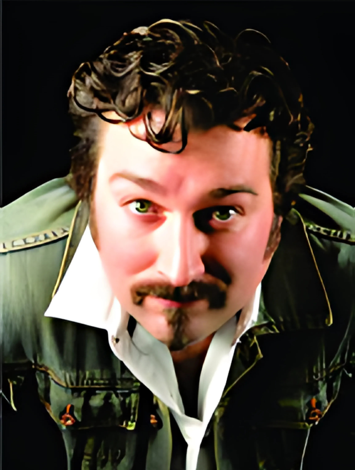 A man with curly hair and a mustache is wearing a green jacket