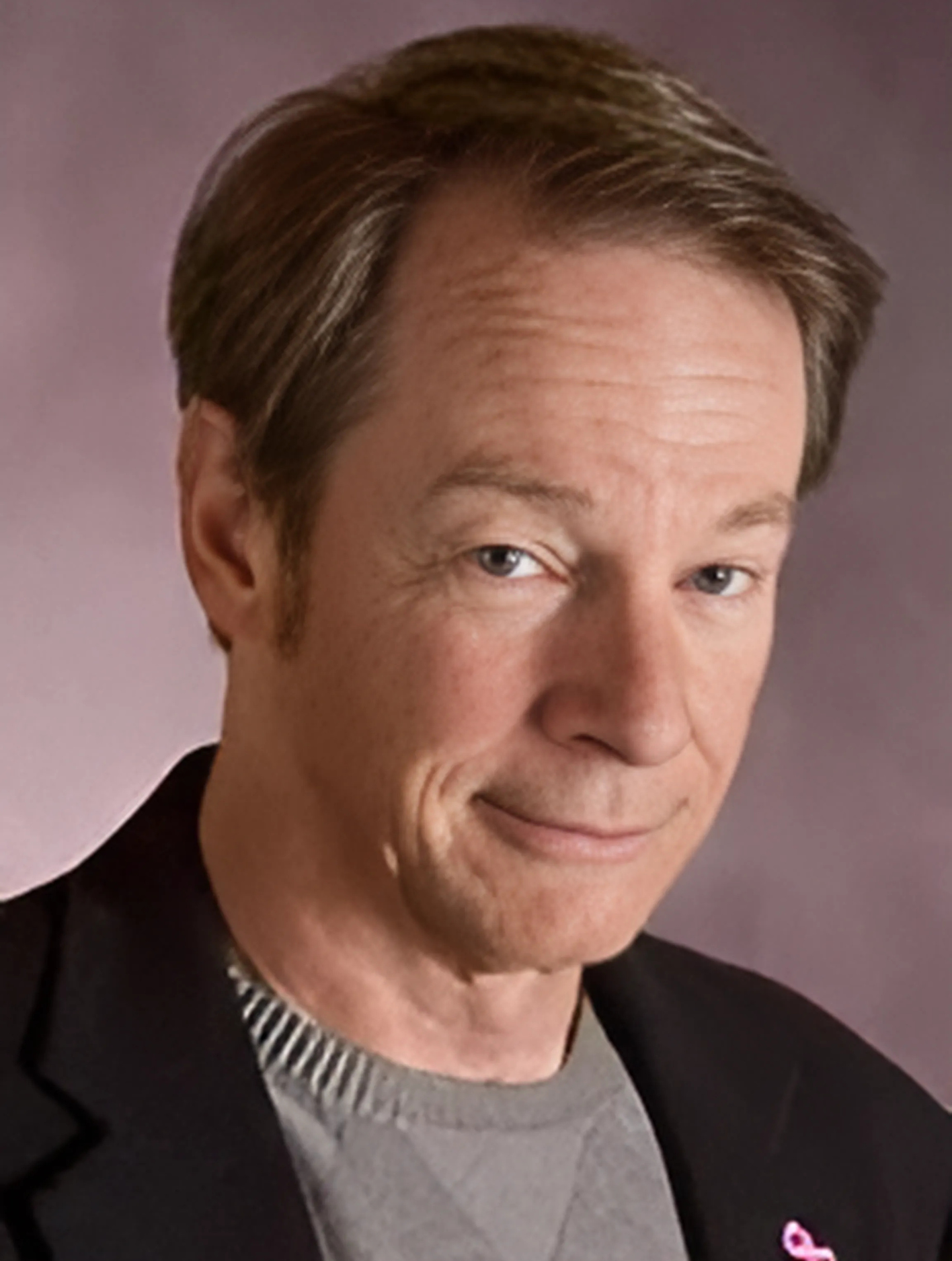 A close up of a man 's face with a pink ribbon on his jacket