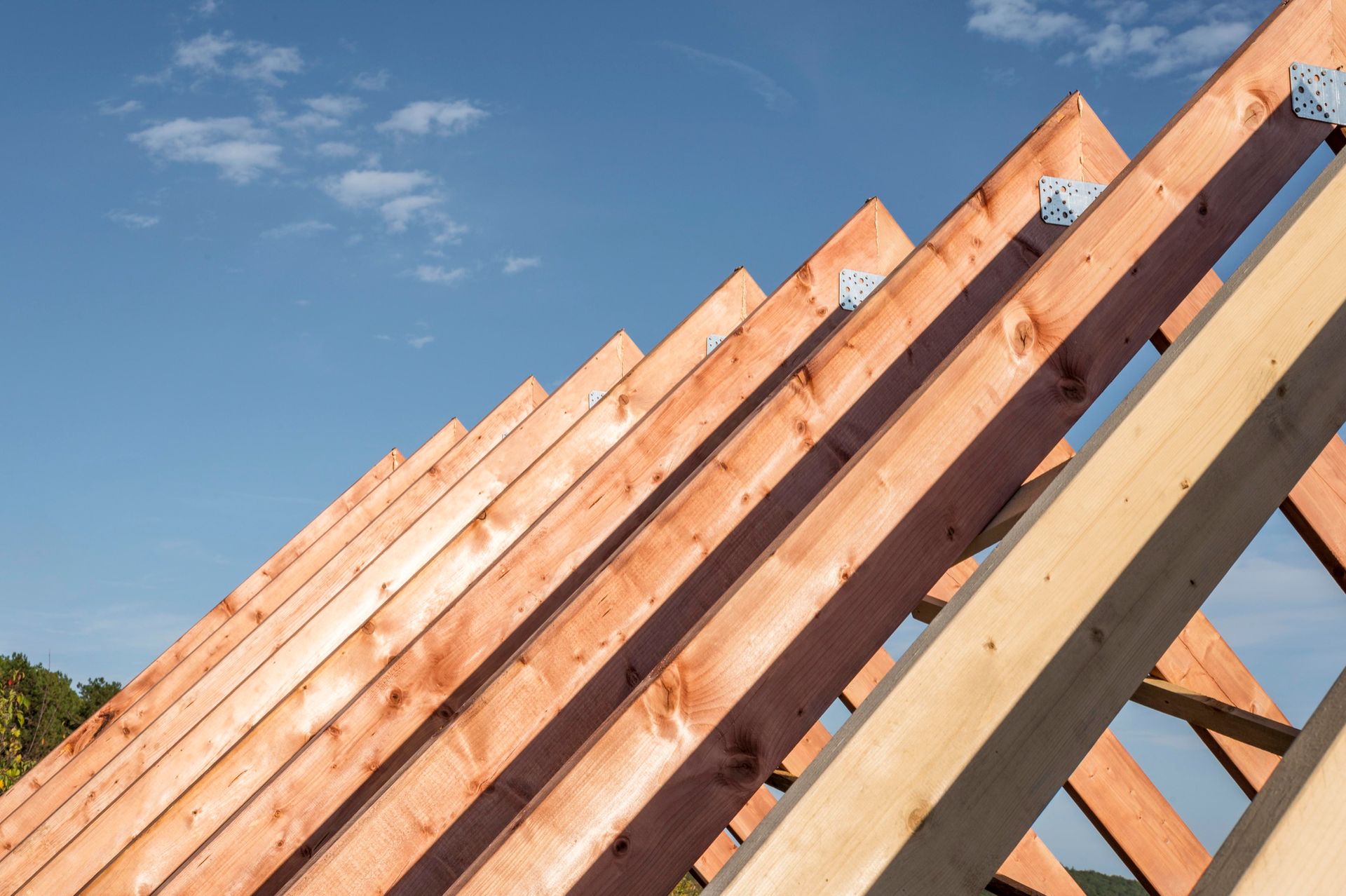 A roof is being built with wooden beams against a blue sky.