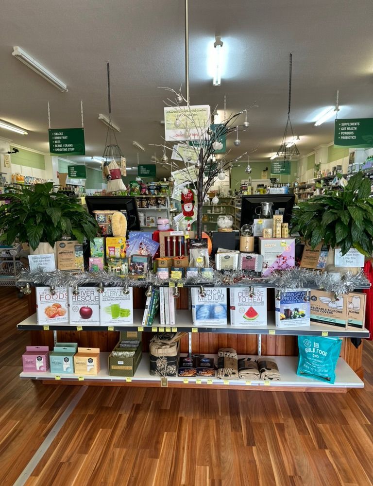 Shelves displaying various packaged products in a brightly lit store, featuring food and gifts. Wooden floor and white shelving — Atherton Health Food Centre in Atherton, QLD