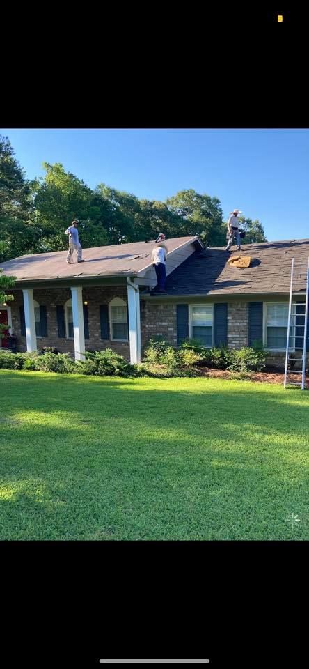 Three workers on a roof of a brick house, working on the roof. Green lawn in the foreground.