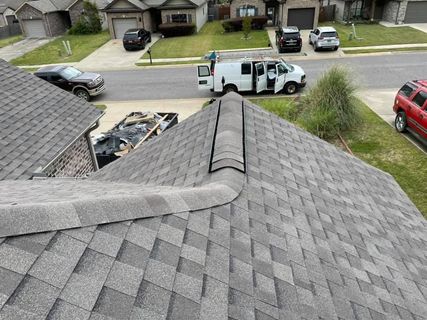 Roof with grey shingles and a van parked in front of houses on a sunny day.