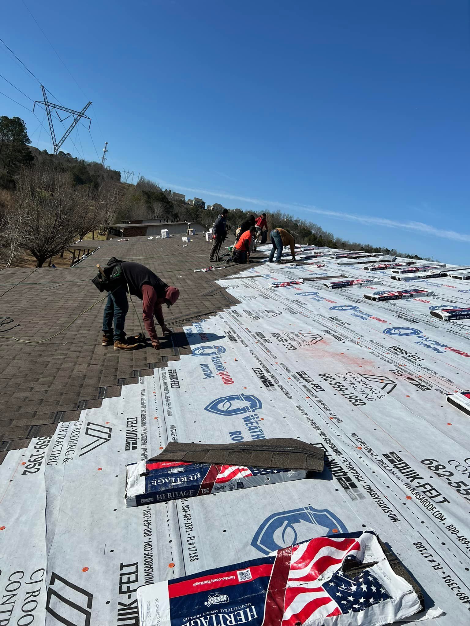 Roofers installing new roofing material on a sloped roof under a clear blue sky.