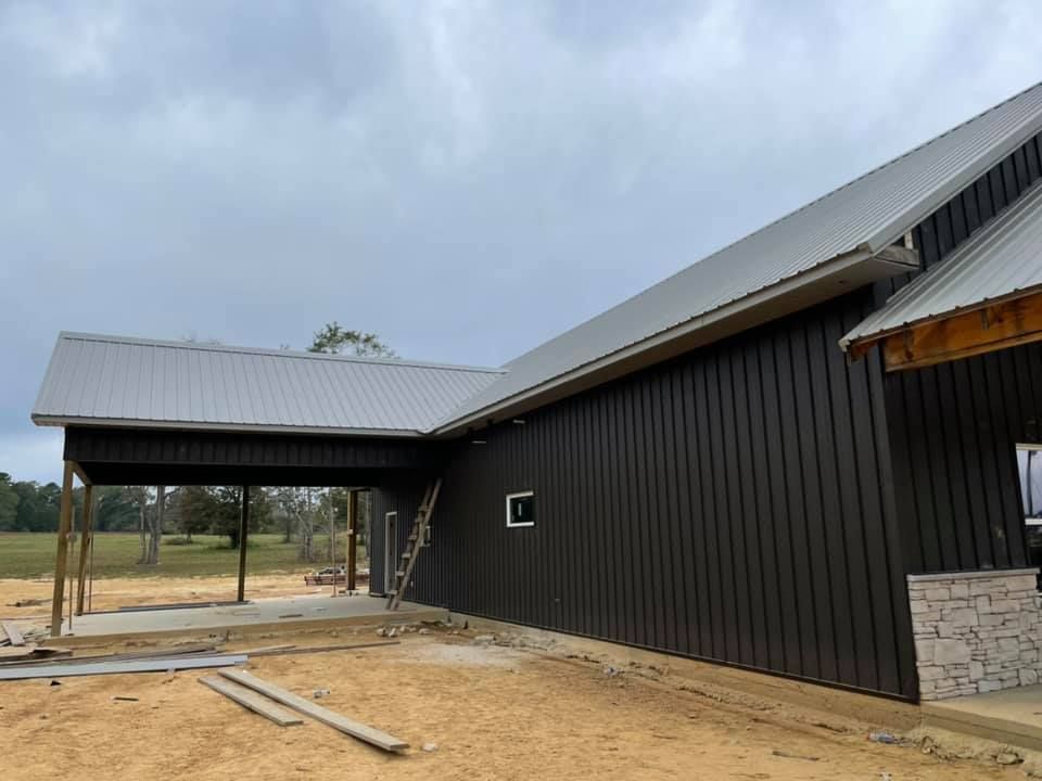 Exterior view of a new building under construction; dark siding, gray roof, covered porch, cloudy sky.